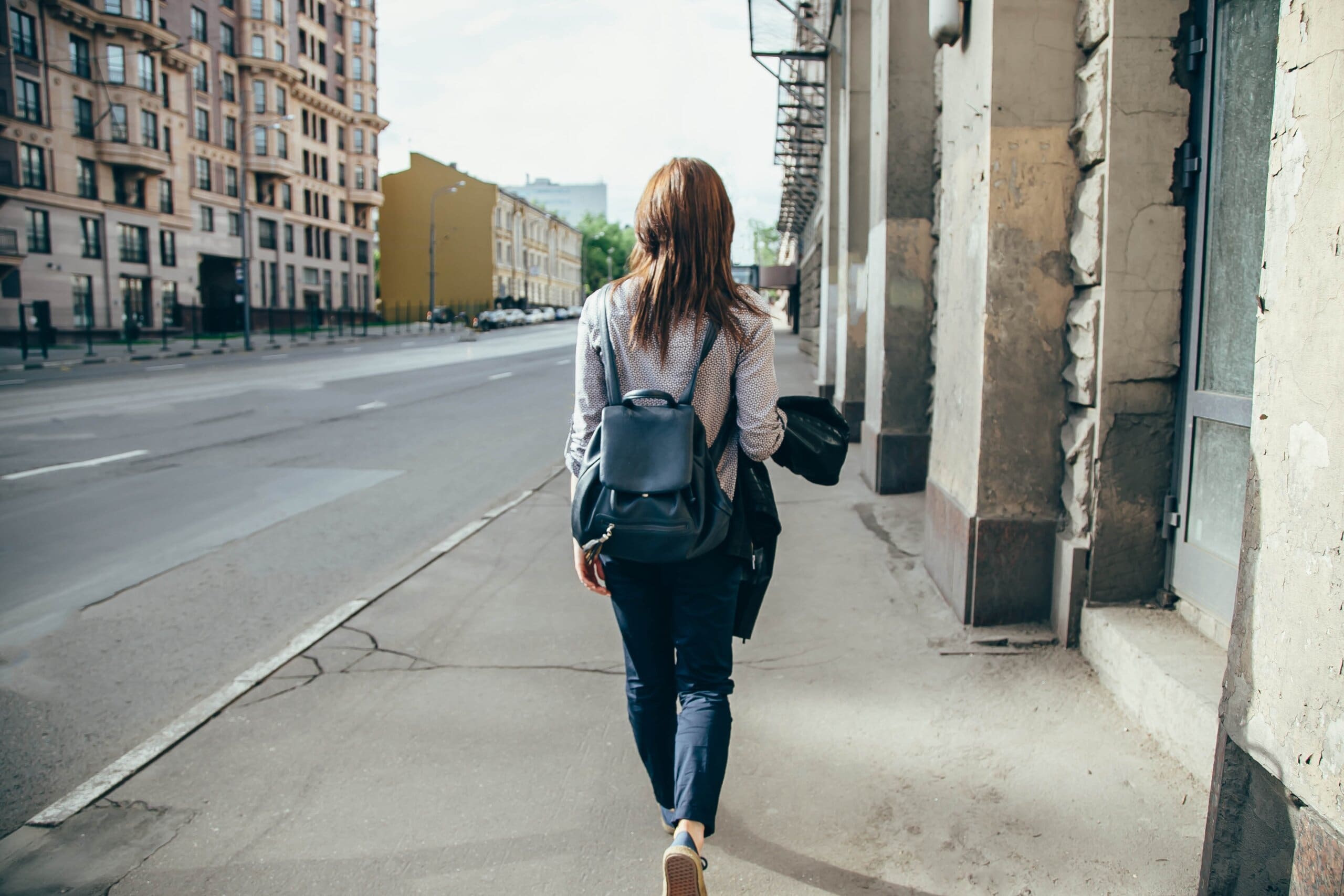 Back view of a girl with a backpack walking through a town street.