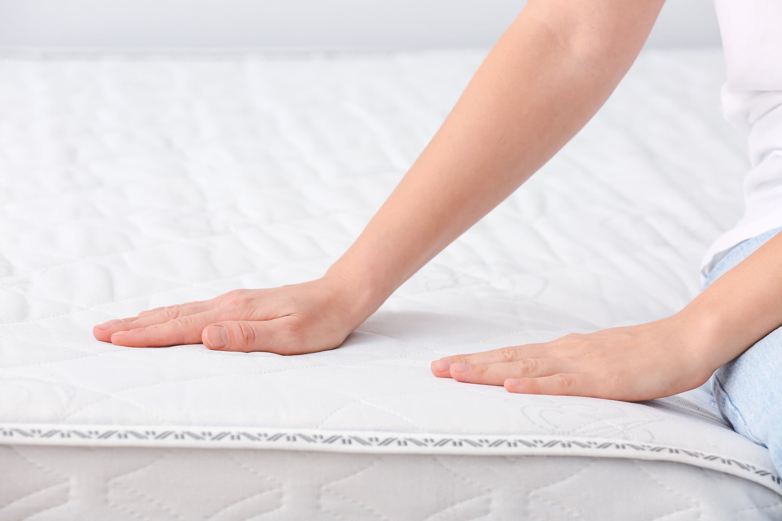 Close up of woman's hands testing the firmness of a mattress as she sits on it.