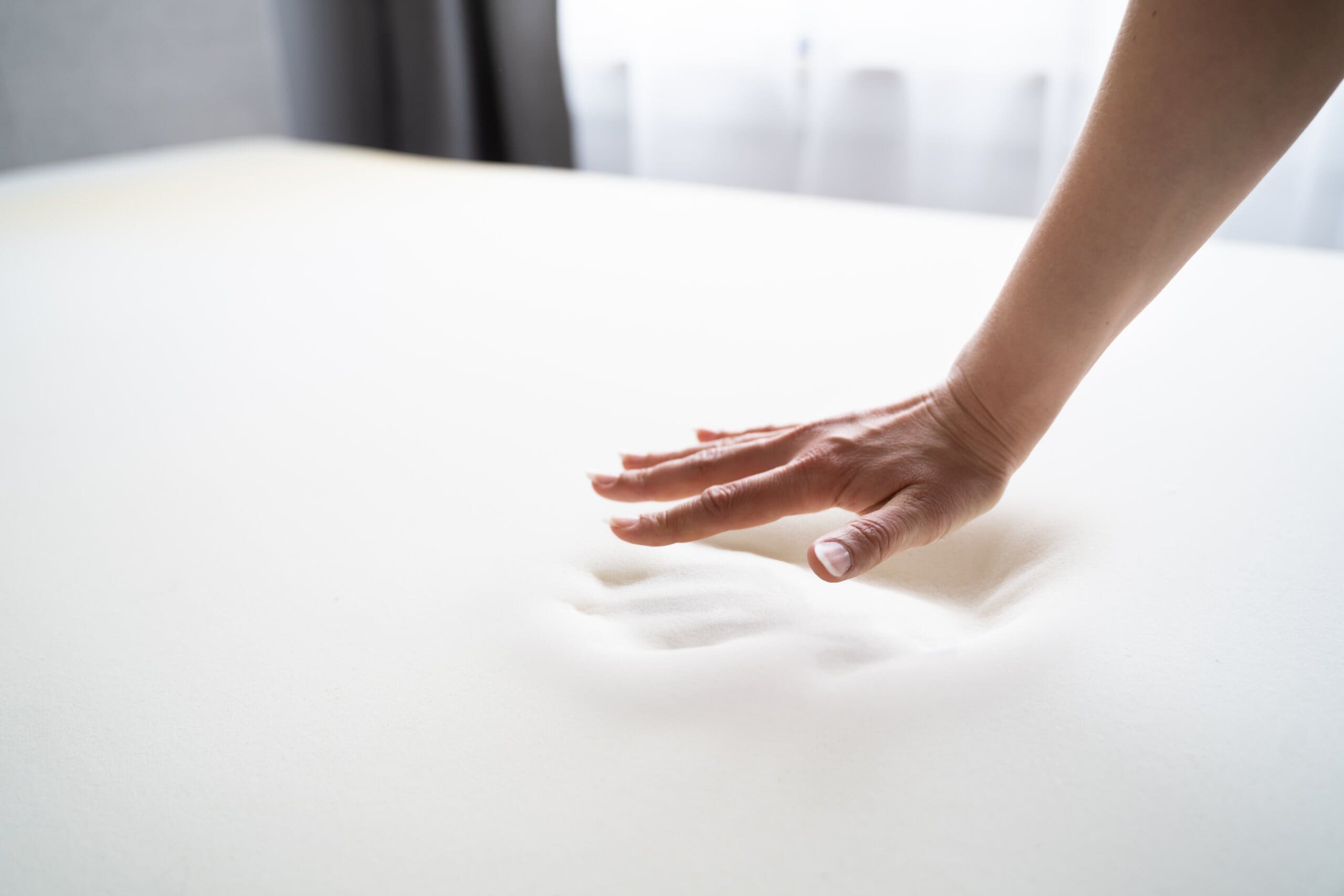 Close up of a hand testing a memory foam mattress, leaving a hand print compression.