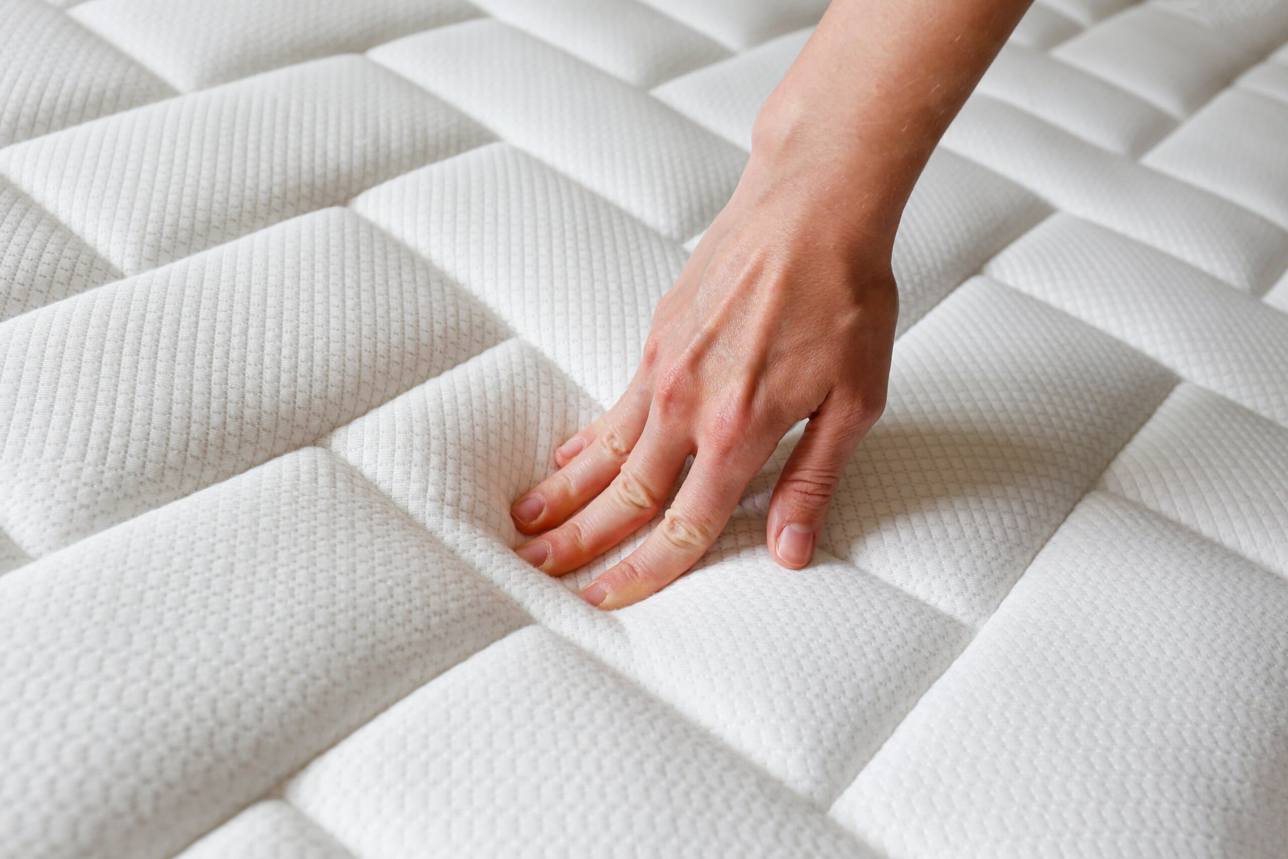 Close up of hand testing the firmness of a mattress surface.