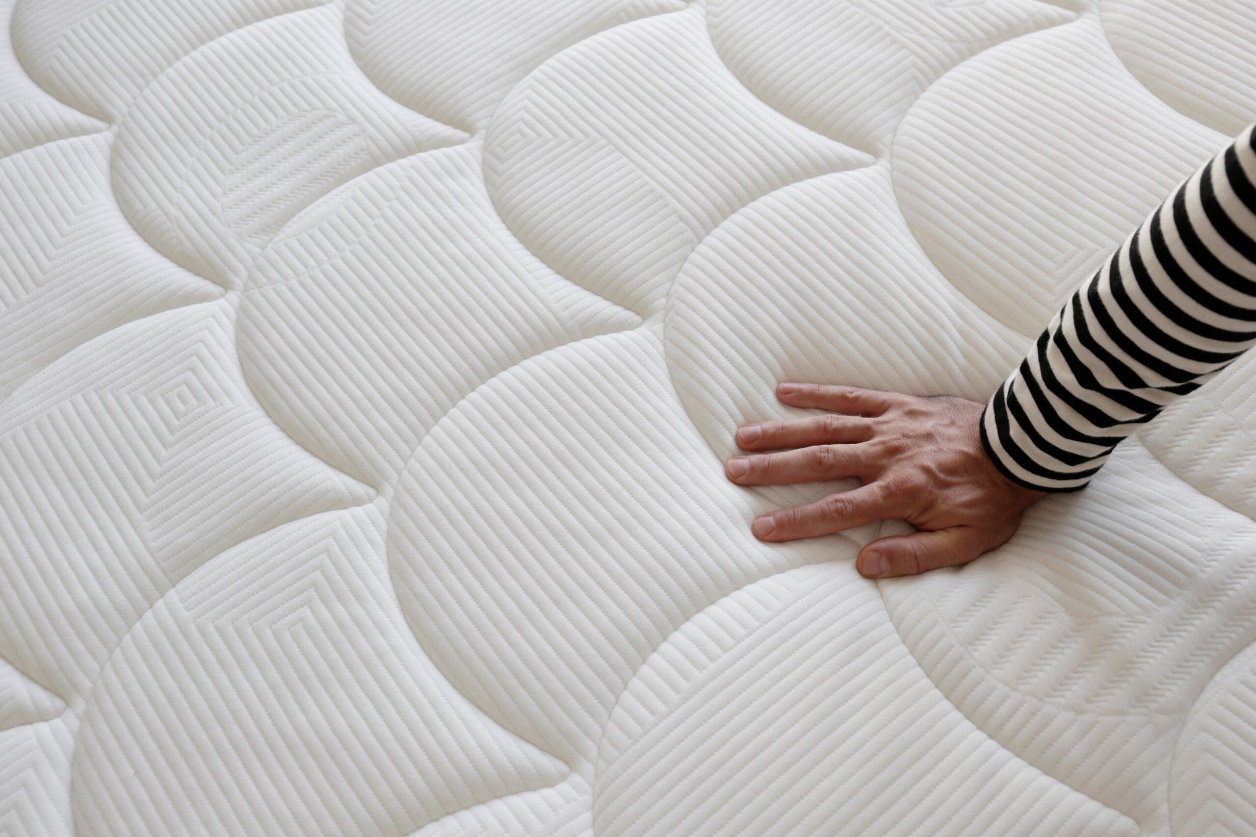 Woman's hand testing the firmness of a mattress.
