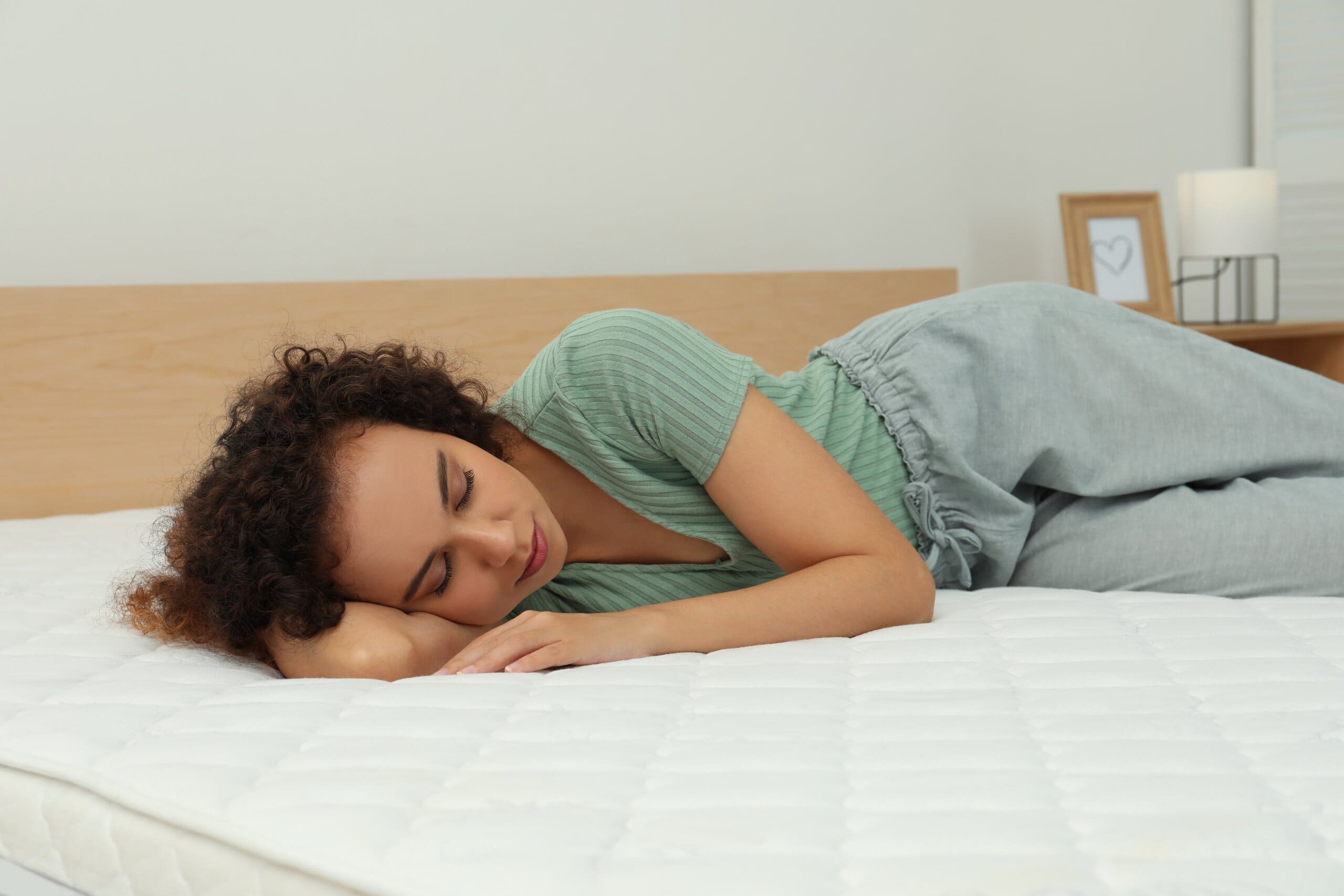 Young woman sleeping on an unmade mattress surface.