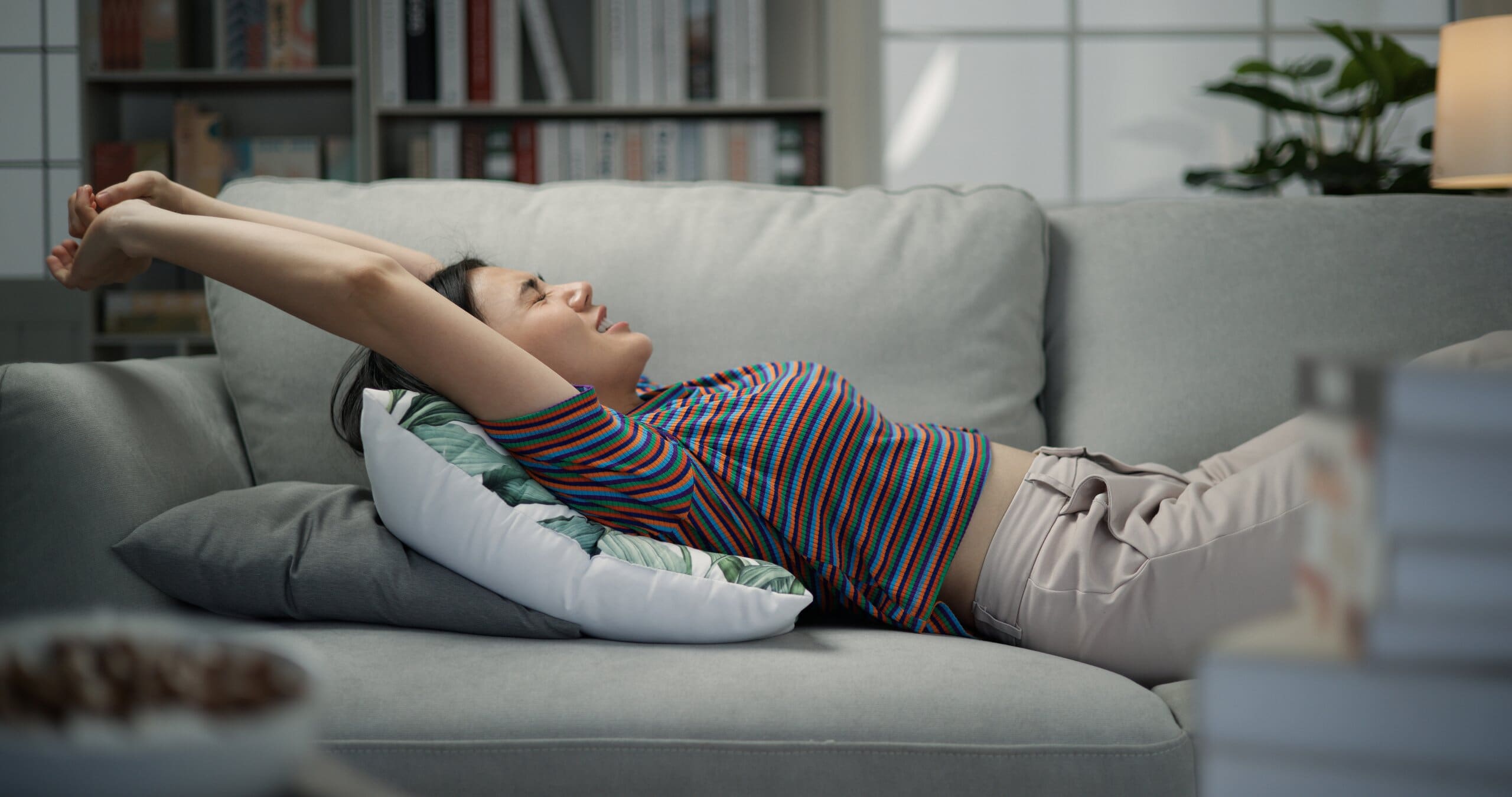 Woman layed stretching out on a sofa with pillows under her.