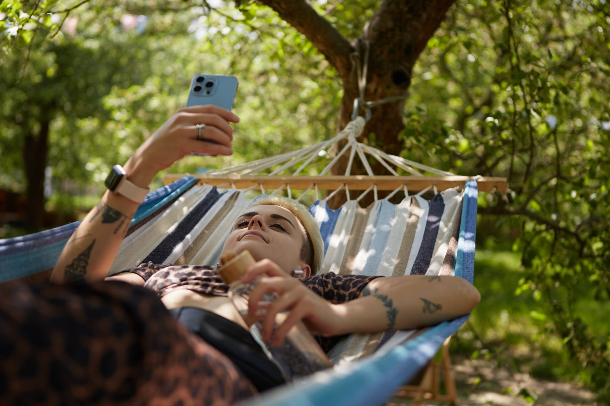 Young woman with tattoos on her phone in a garden hammock.