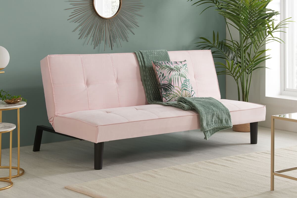 Pink sofa bed with green blanket and pillow, in a modern room.