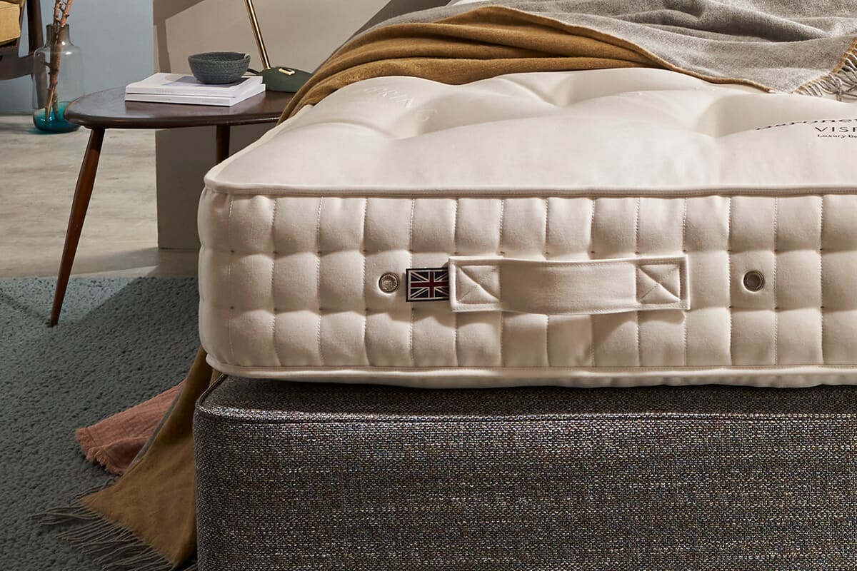 The bottom corner of the vispring baronet mattress on a grey divan bed with bedroom furniture in the background.
