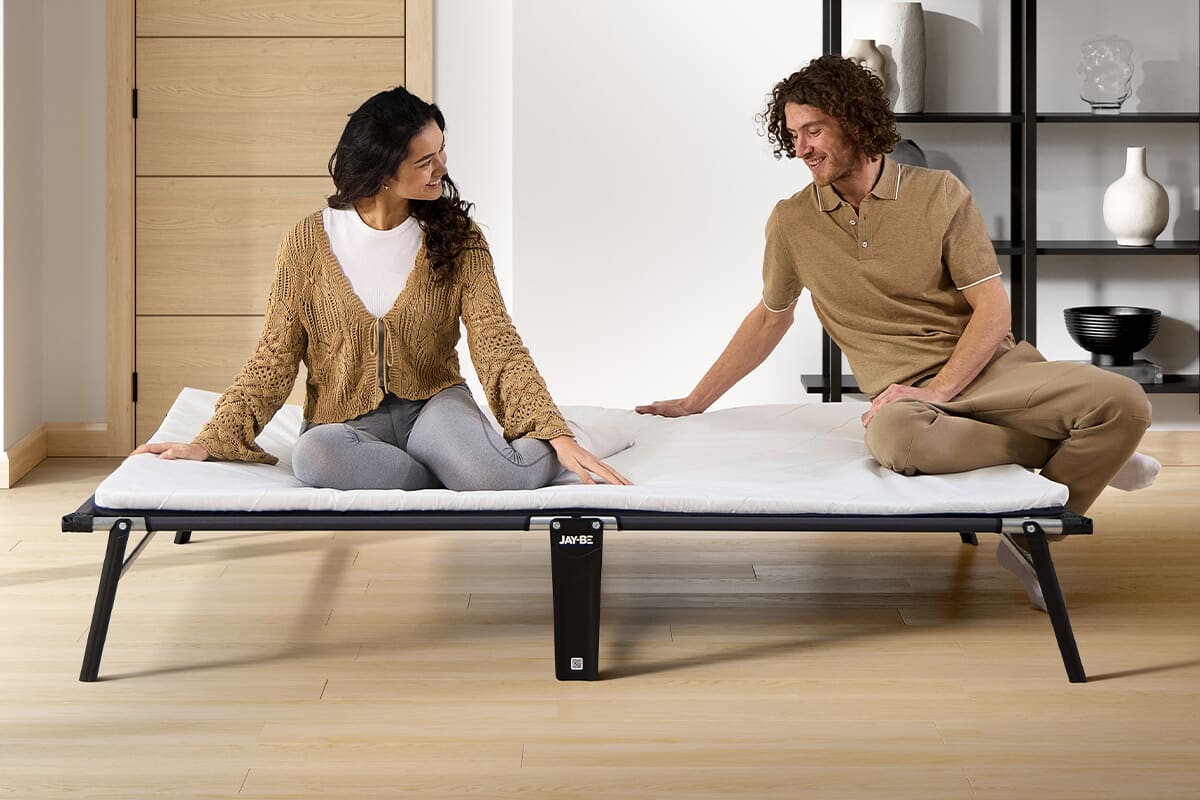 Man and woman sitting on a folded out small double folding bed.