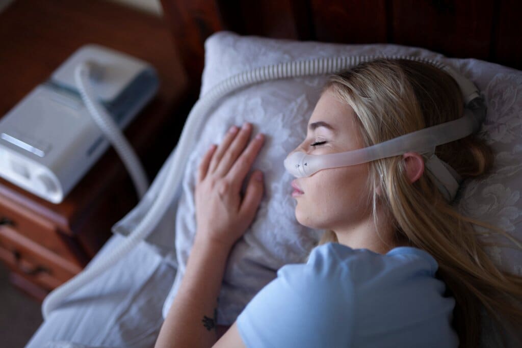 Young woman sleeping in bed with a CPAP machine and mask on.