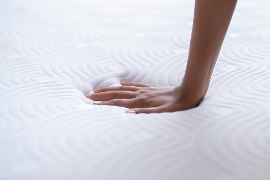 A person's hand pressing down onto a memory foam mattress, leaving a hand print.