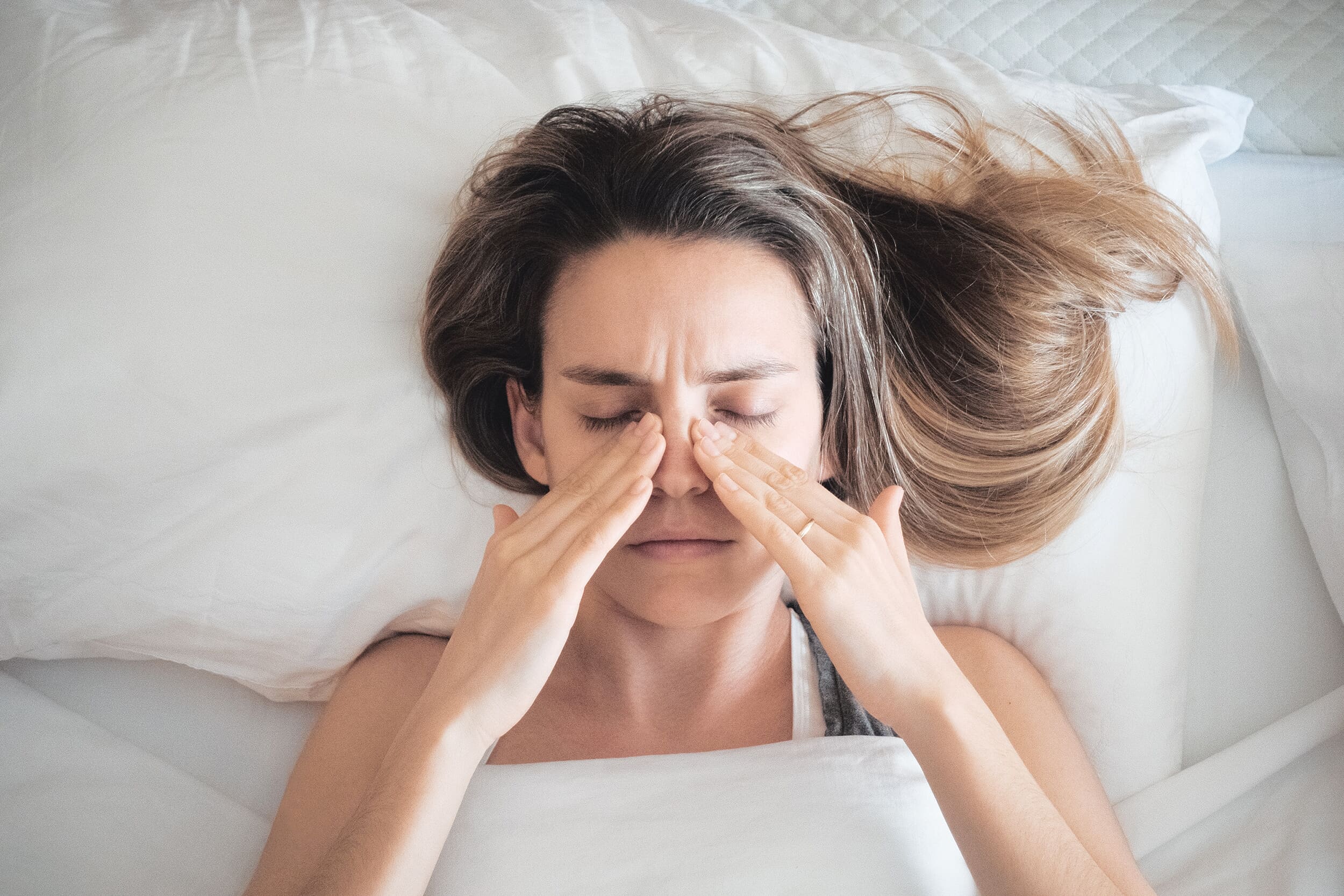 Close up of woman with her hands by her nose, signally blocked sinuses due to sleeping with a fan on.