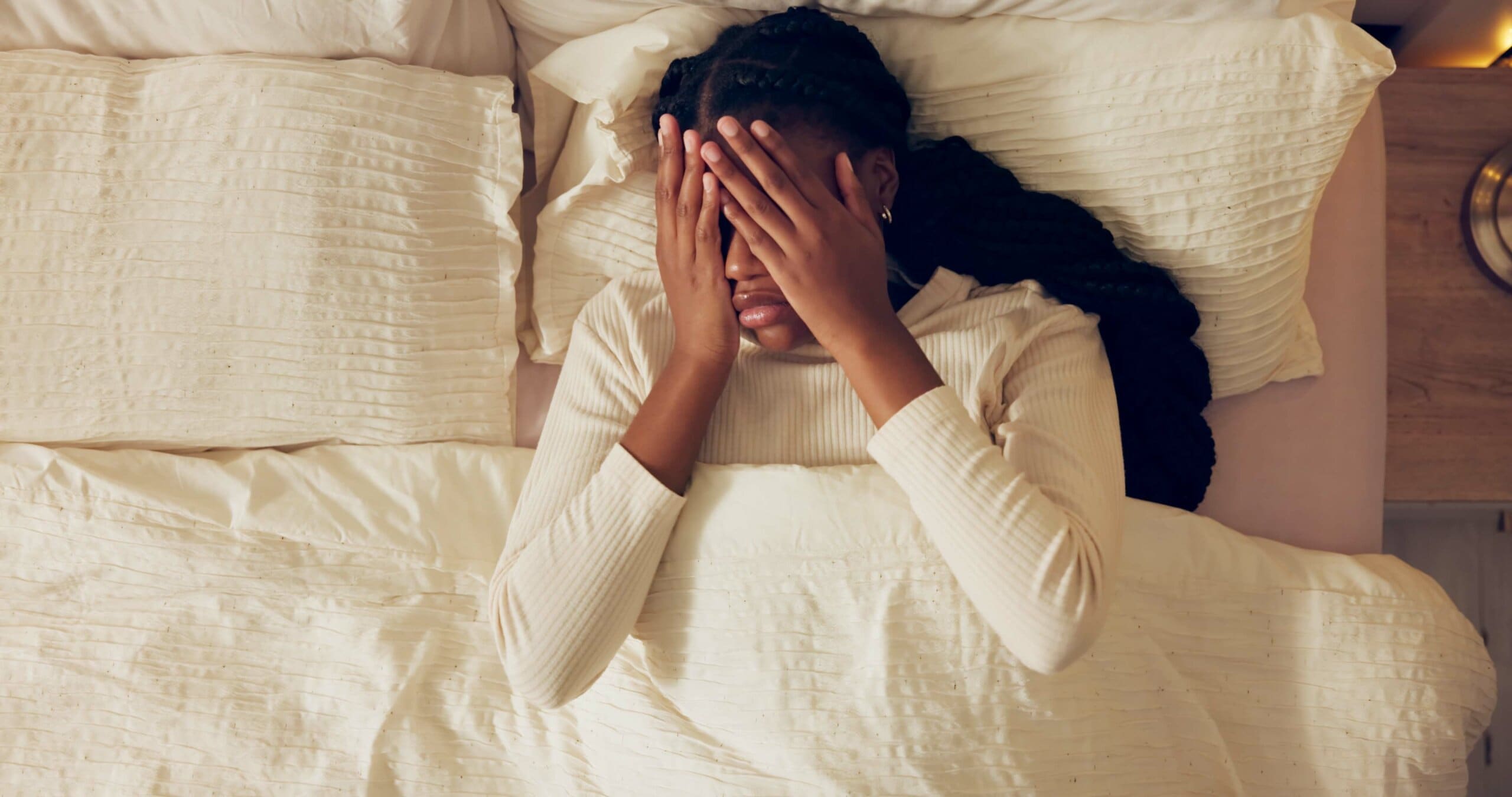 Woman upset in bed with her hands over her face.