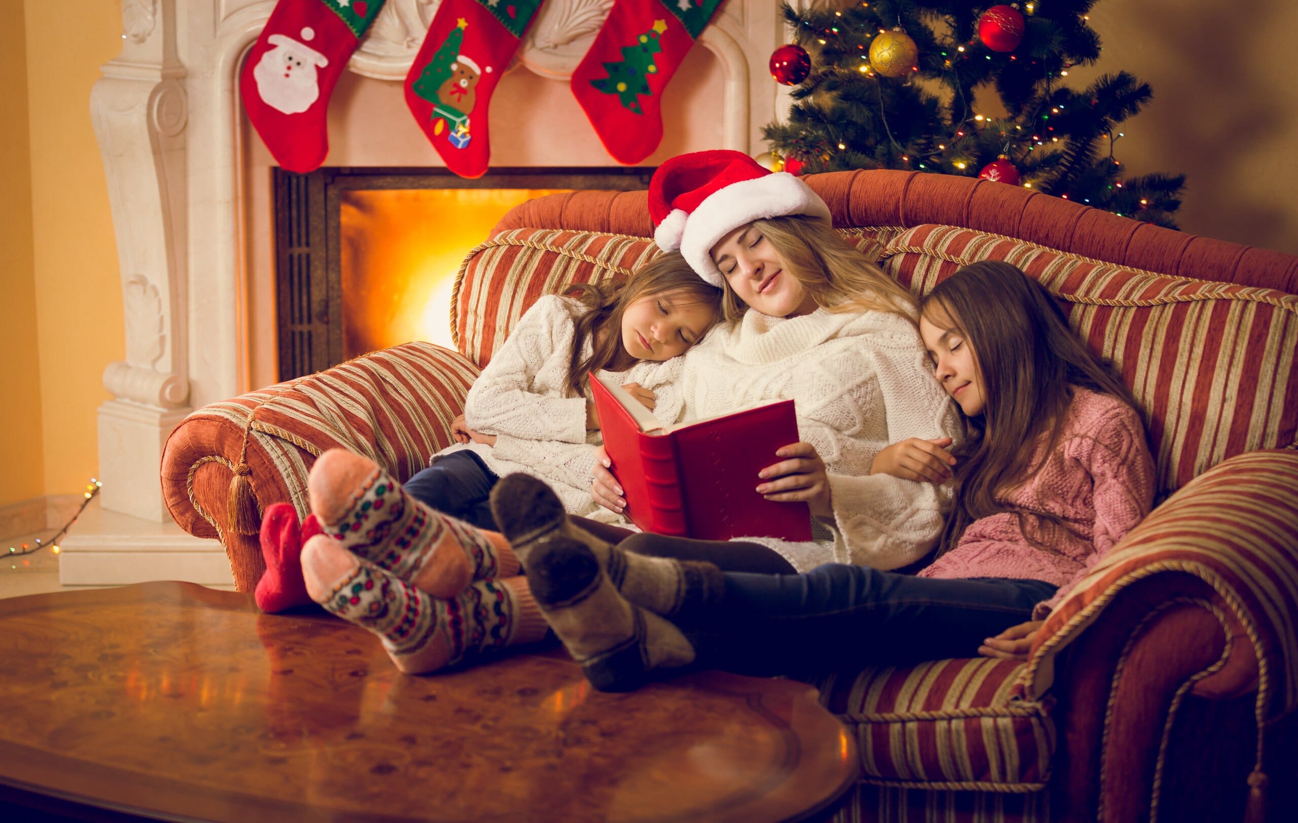 Mother and two daughters  asleep on the sofa at Christmas reading a book.