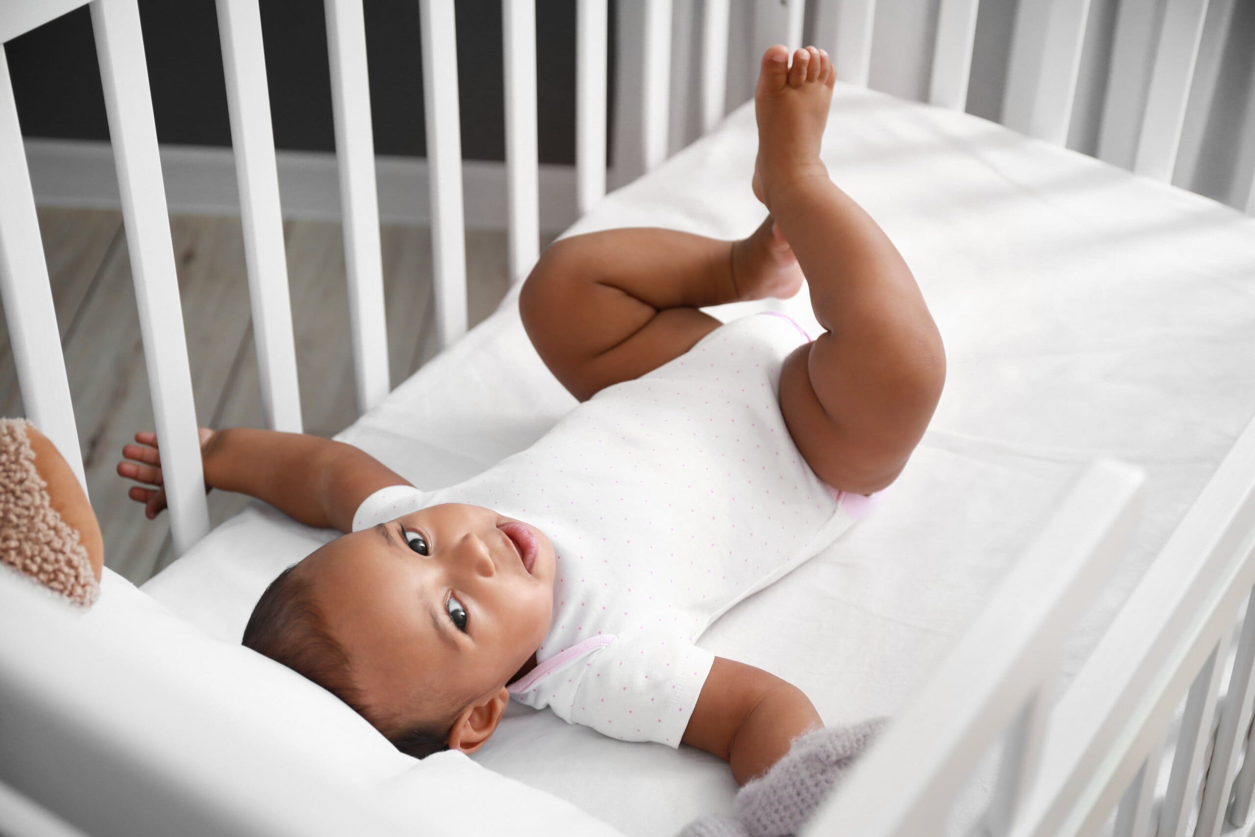 Baby smiling laying in white cot.