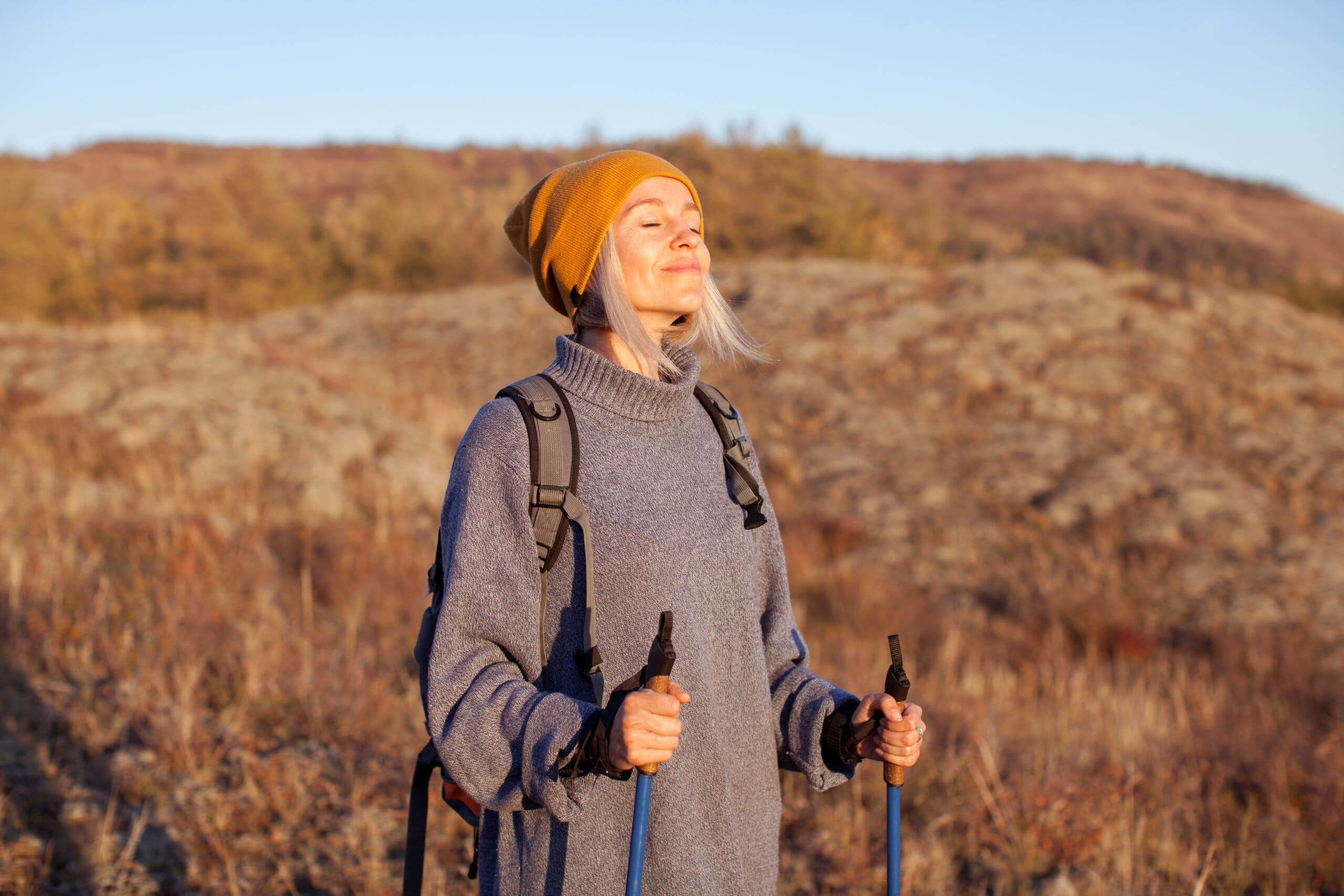 A woman on a hike with walking sticks smiling with her eyes closed.
