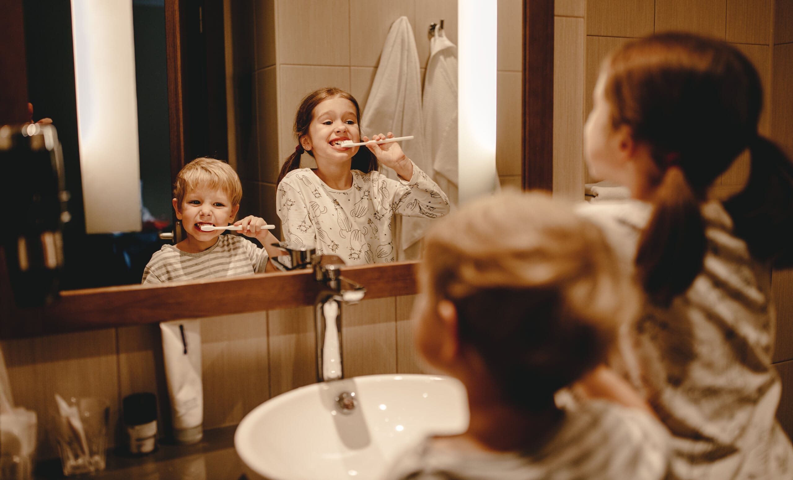 Young girl and boy burshing their teeth in a bathroom mirror.