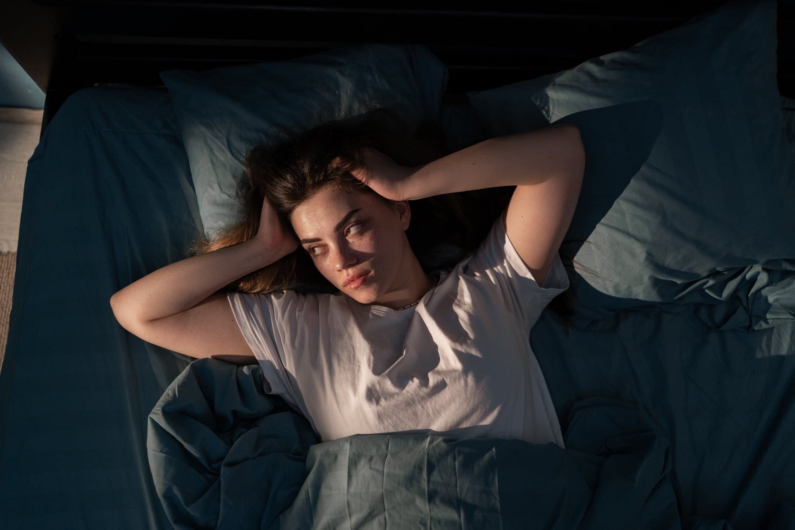 Woman laying in bed with her hands on her head looking stressed.