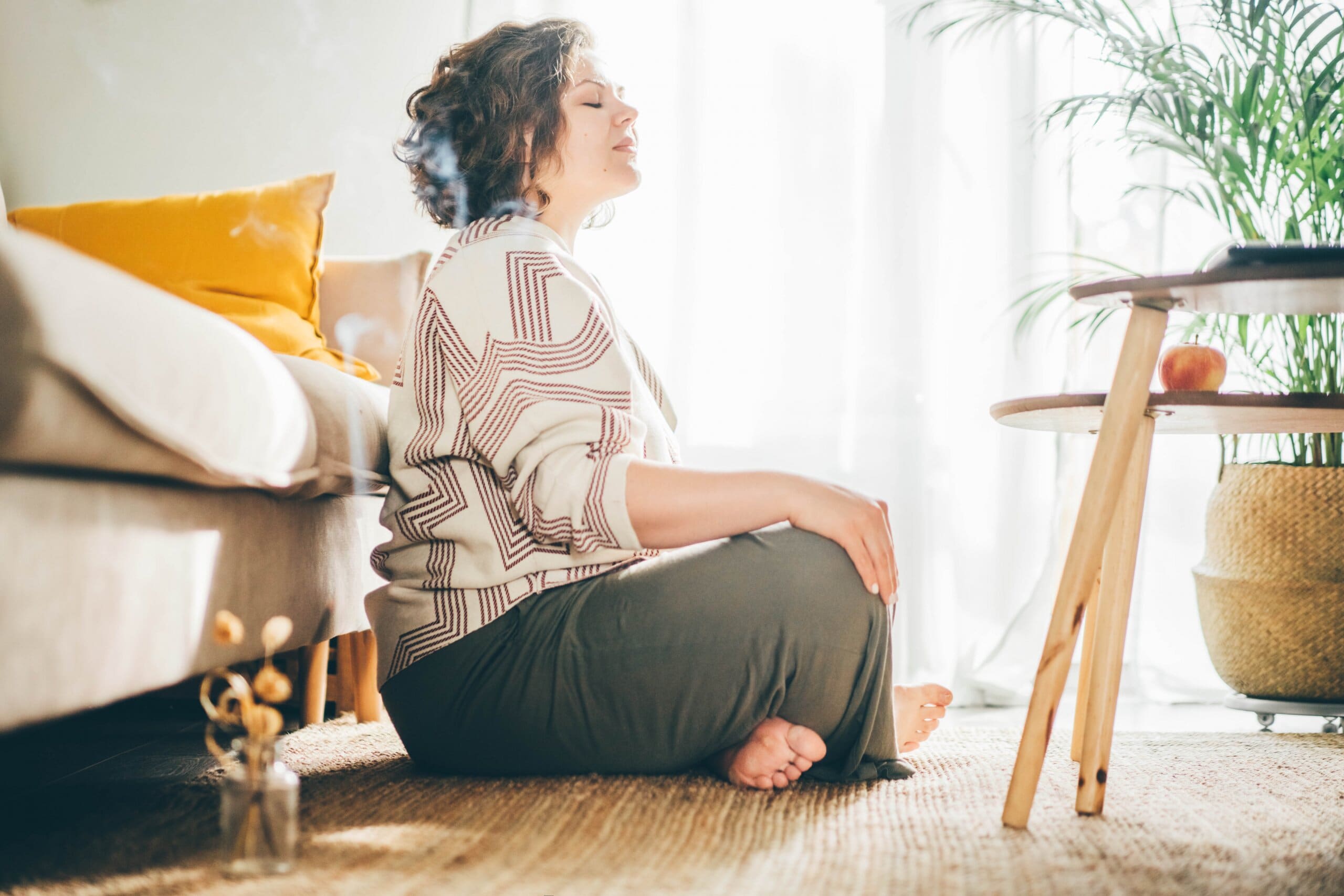 Woman sat cross legged meditating in her bohemian home.