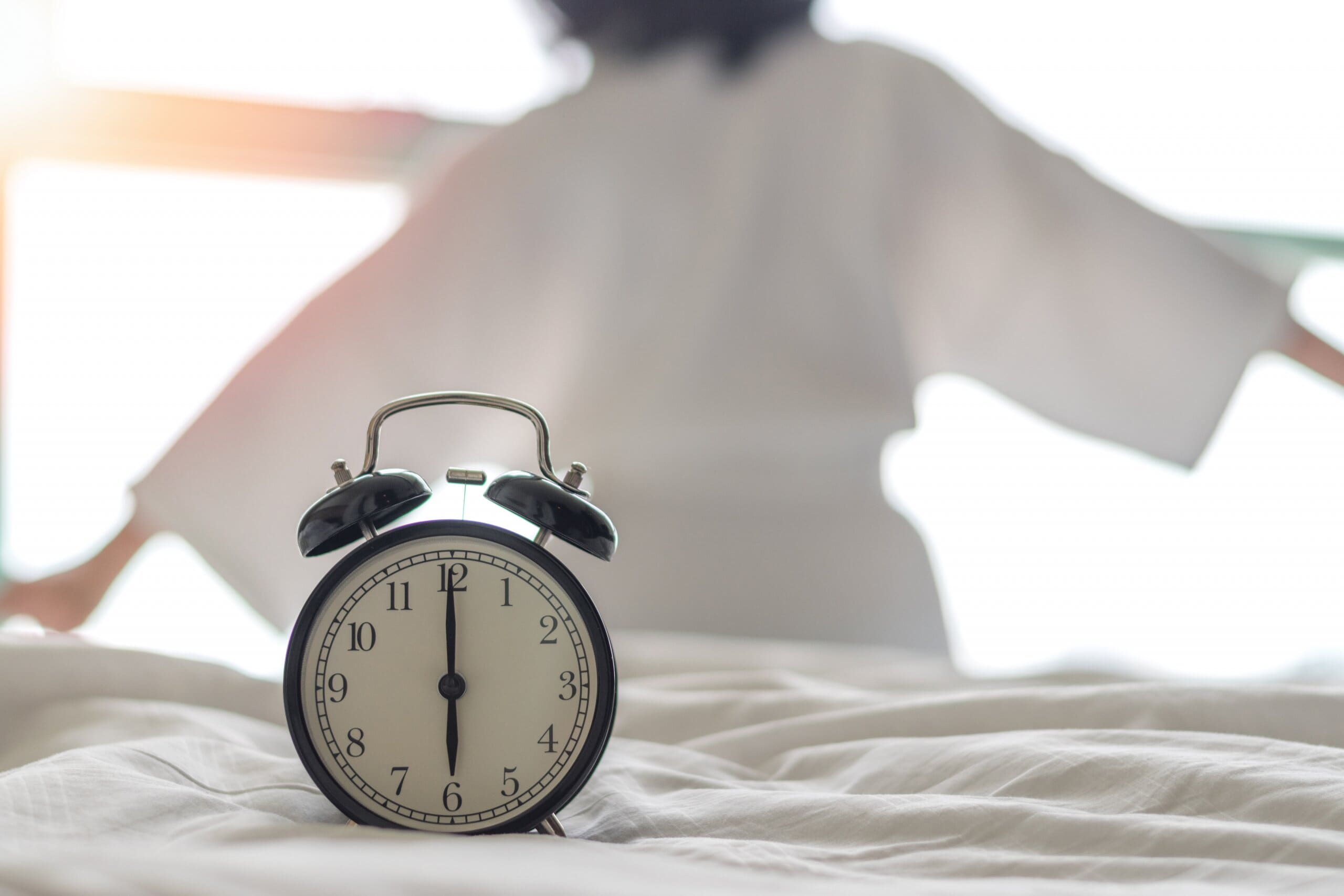 Woman on bed wake up stretching in bedroom with alarm clock at 6 am.
