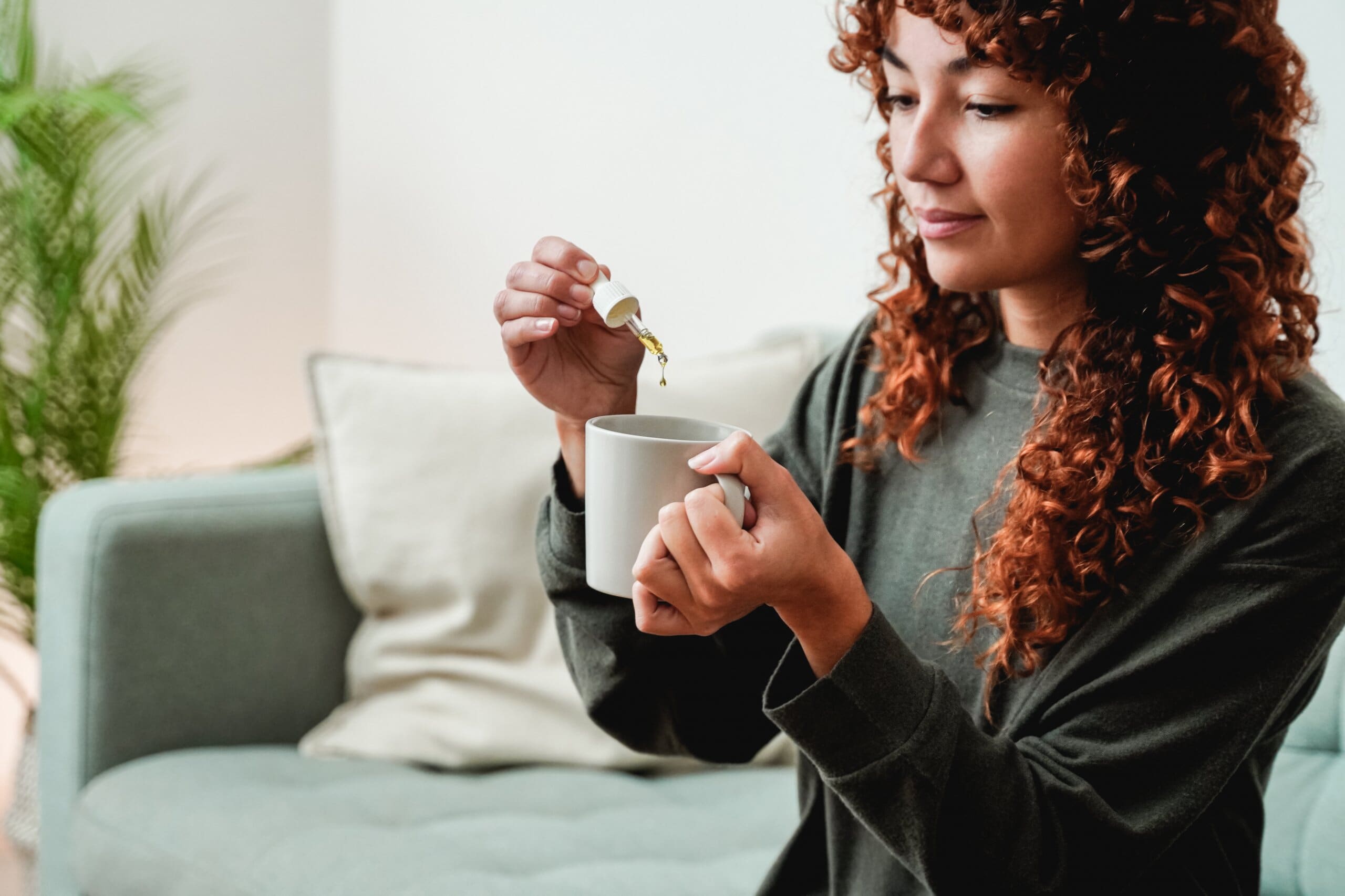 Woman dropping CBD oil into a hot drink.