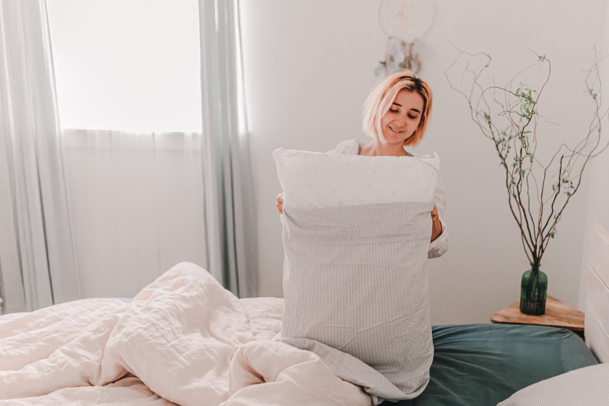 Woman smiling making her bed, putting new pillowcases on.