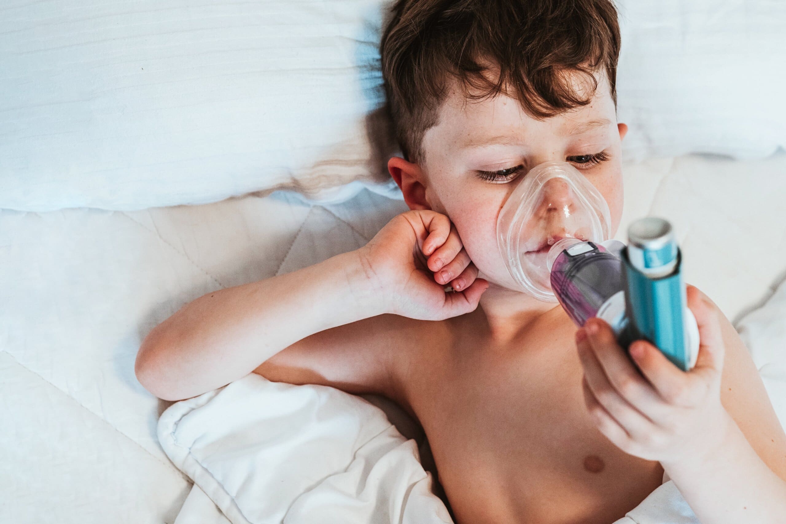 Young boy in bed using an inhaler.