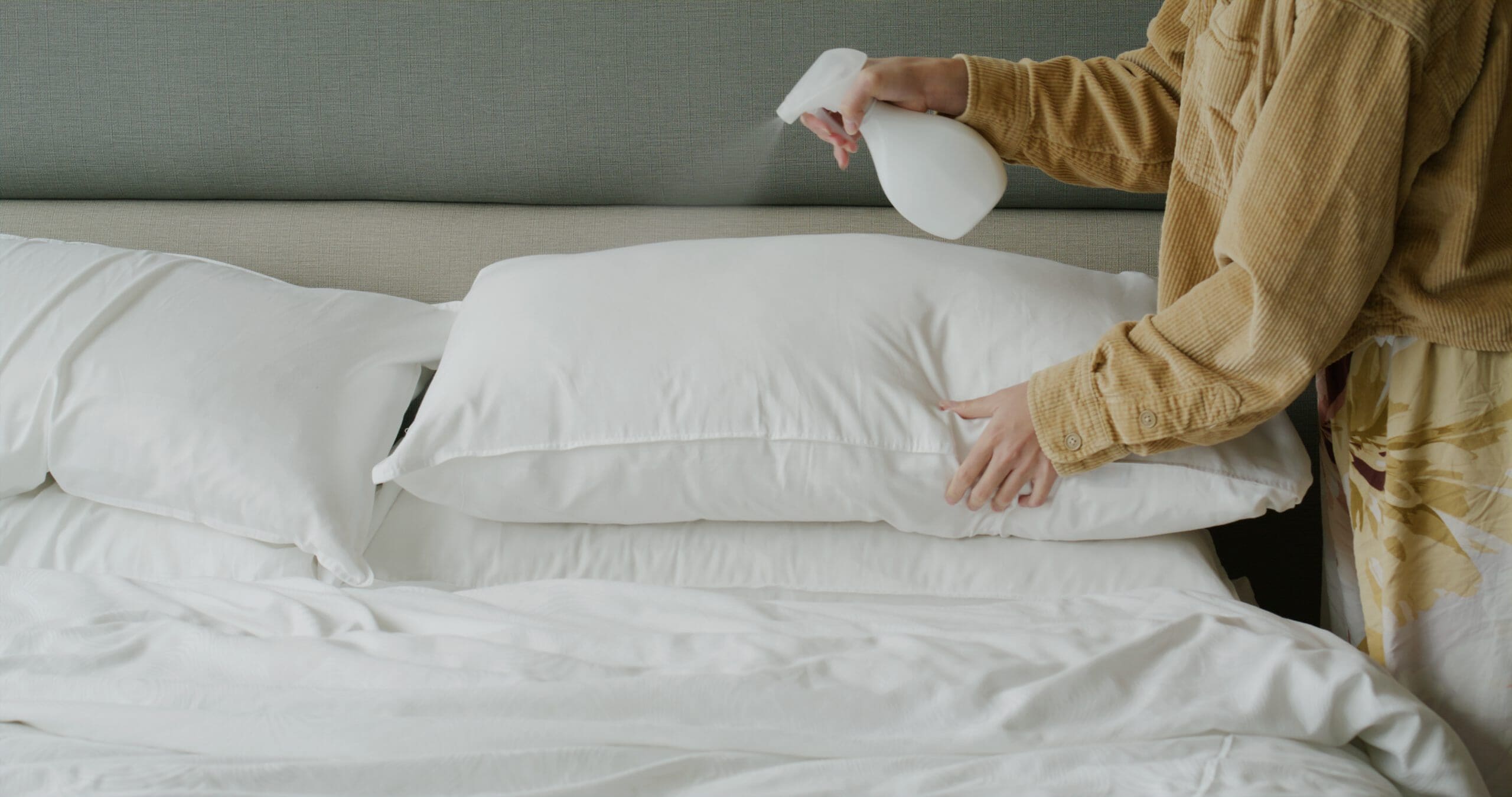 Woman using a spray bottle to clean the top section of a bed.