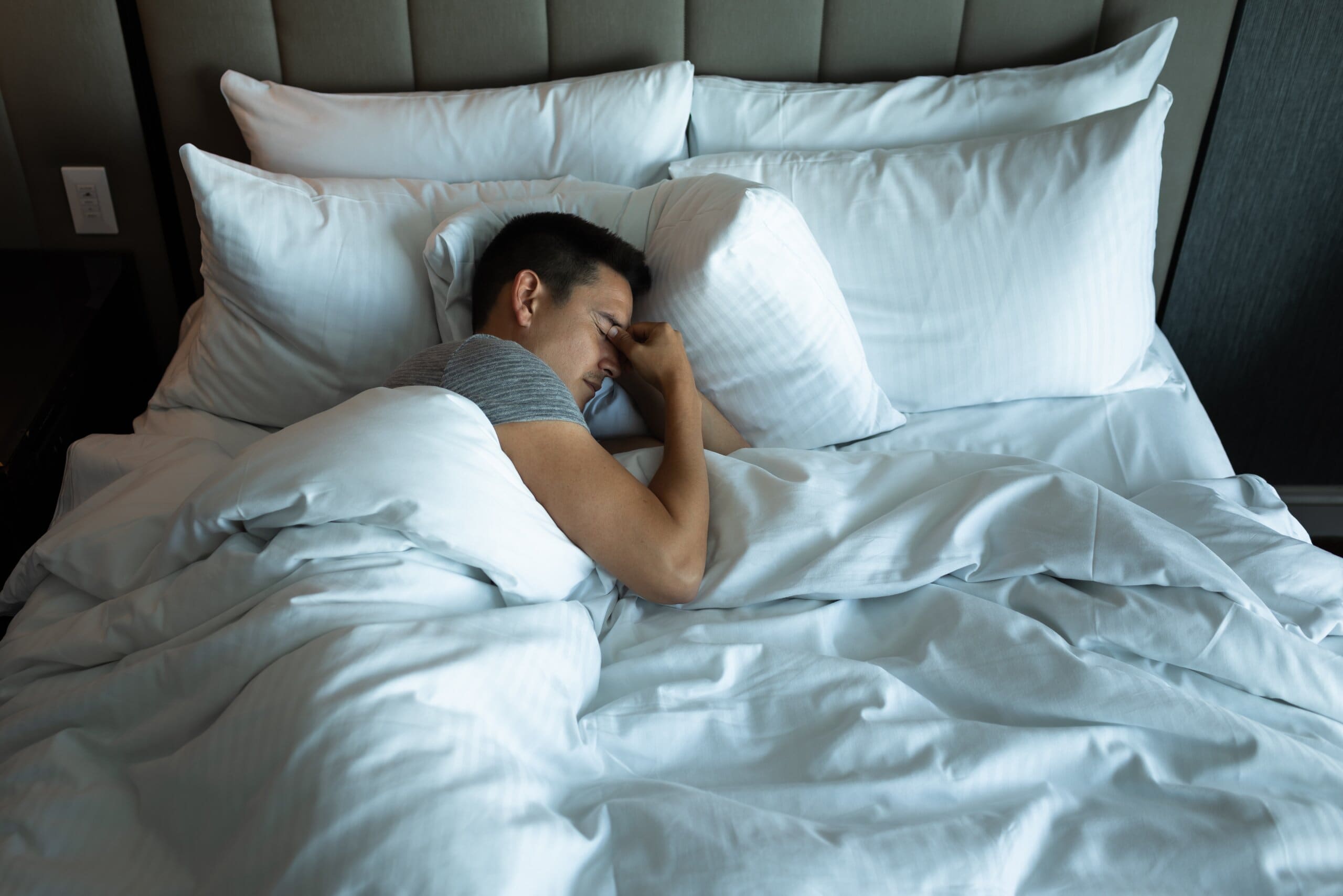 Man holding the bridge of his nose in bed looking stressed.