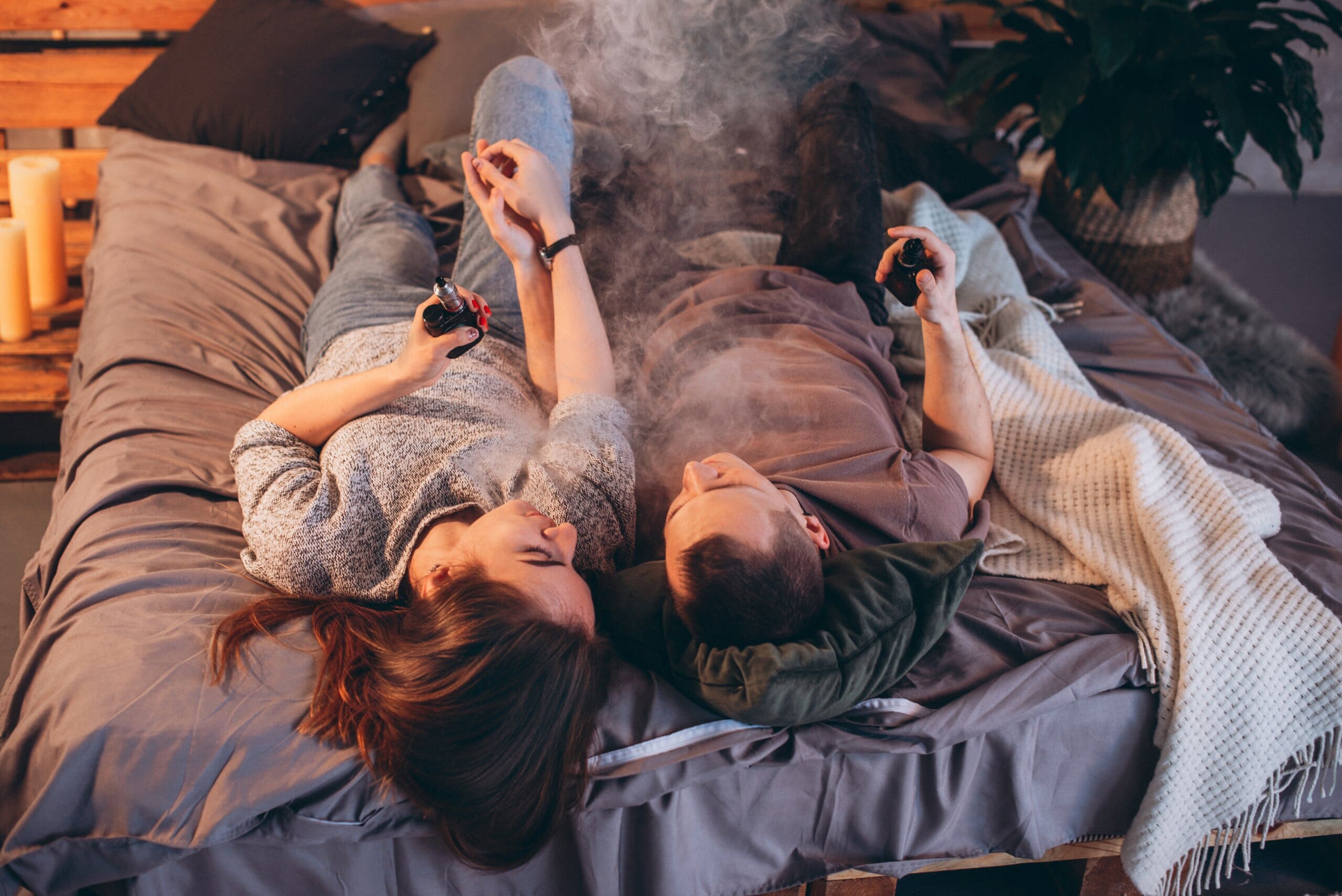 Man and woman smoking vapes in bed.