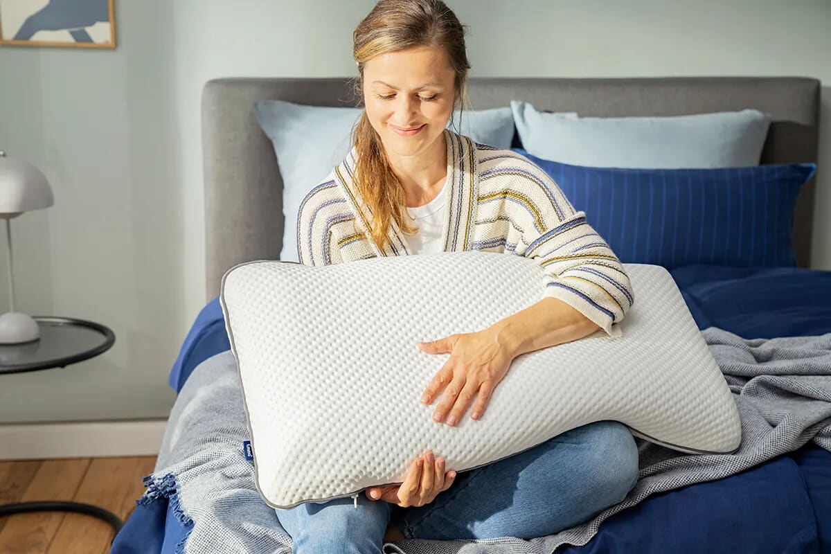 Woman sat on bed holding an Emma pillow.