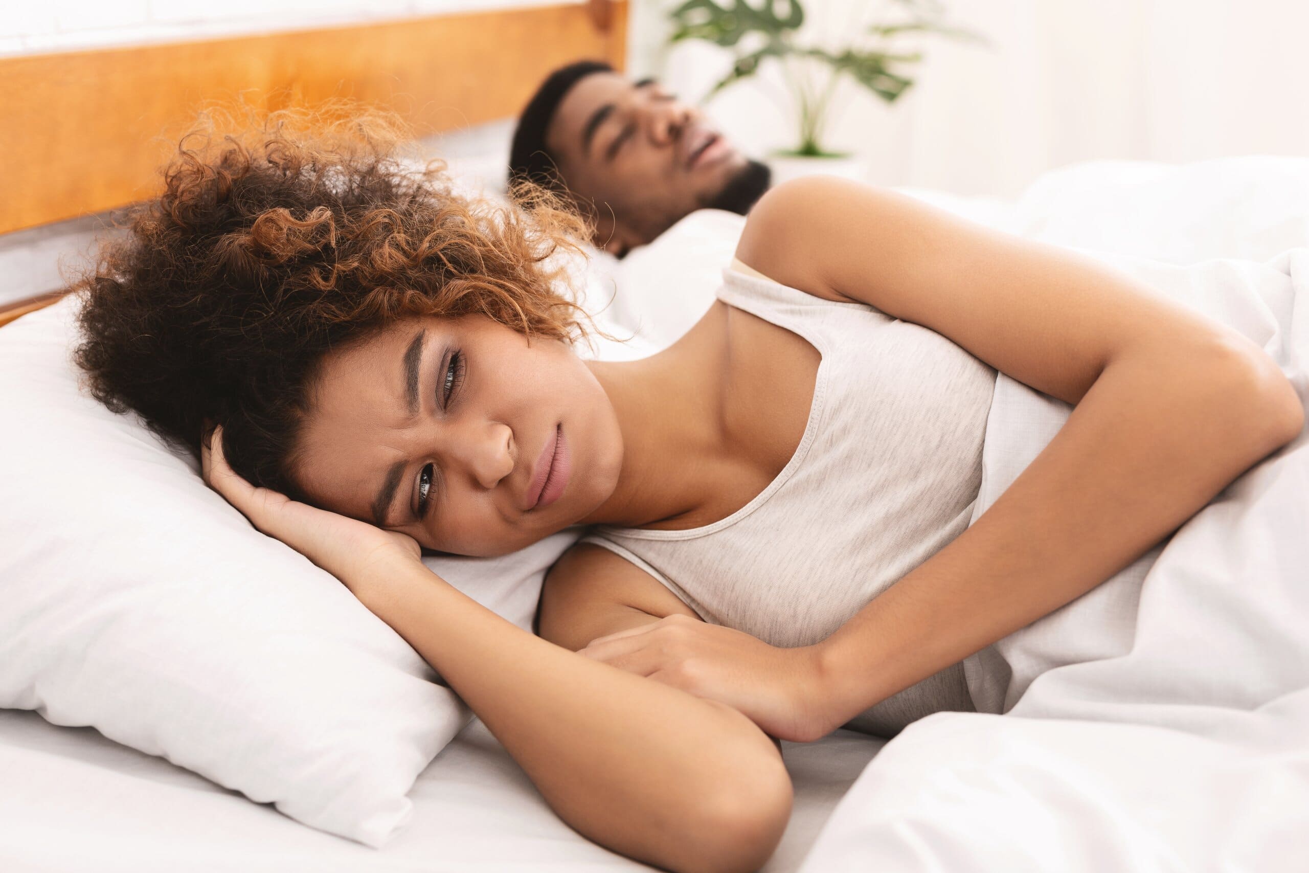 Woman looking annoyed as her partner sleeps next to her snoring.