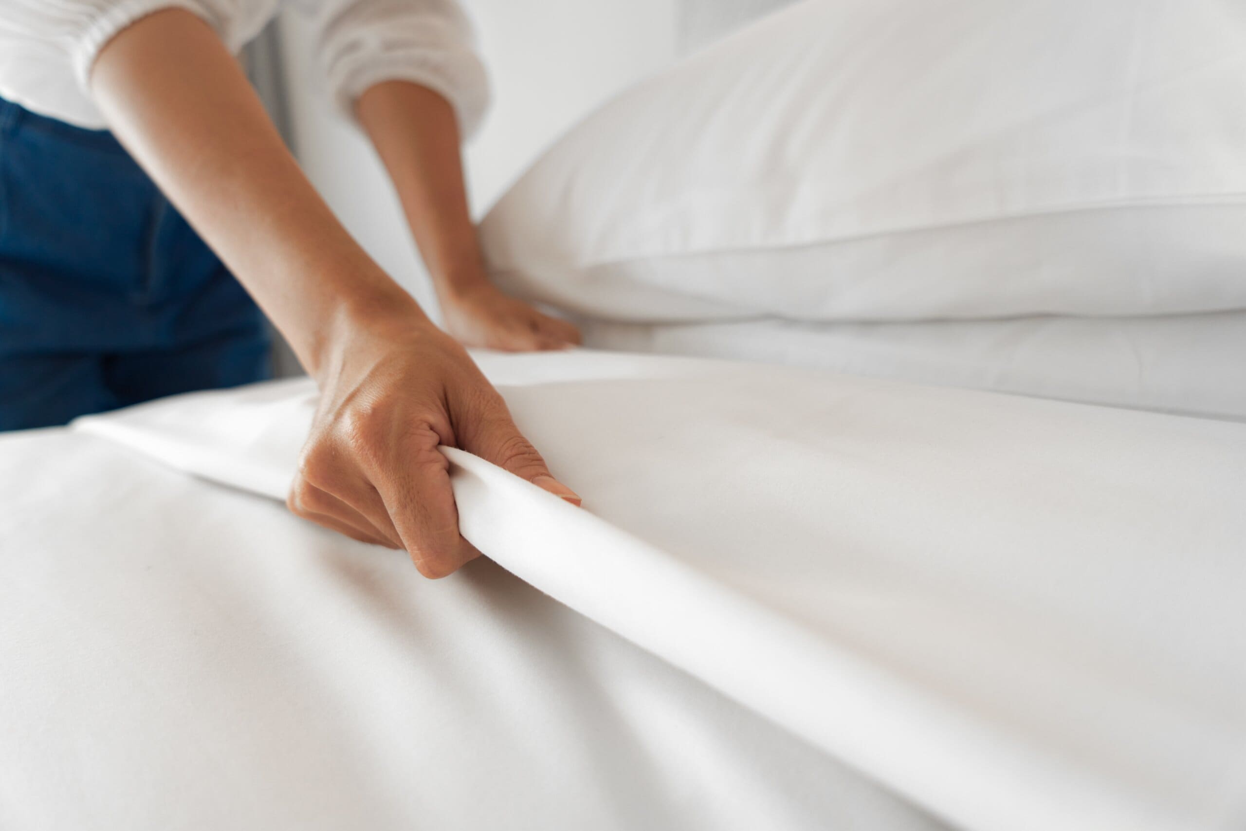 Close up of female hands fixing a white bed sheet.