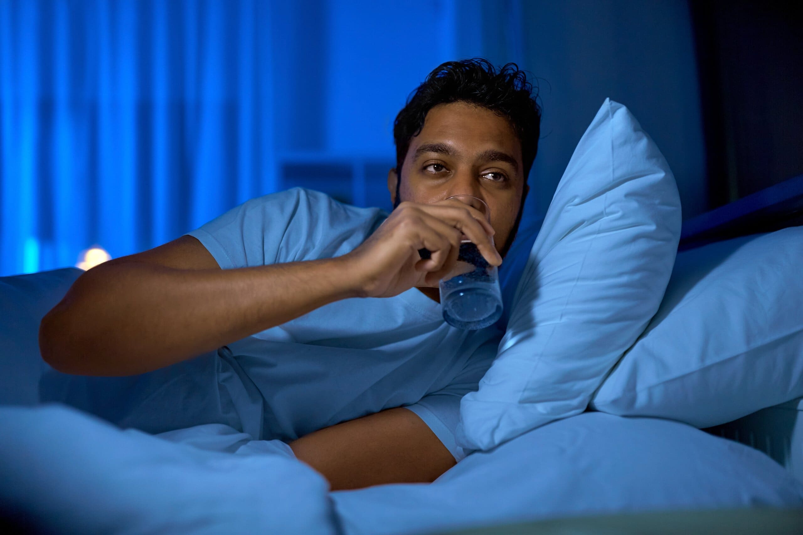 Man drinking a glass of water in bed.
