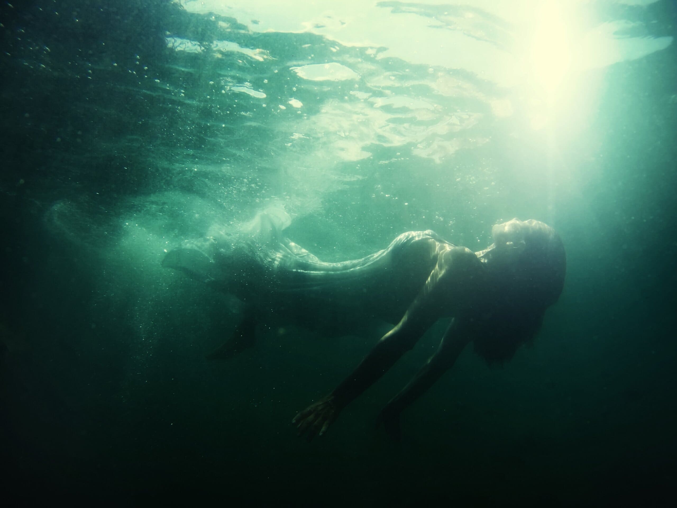 Woman floating underwater in a long white dress. Depiction of drowning.