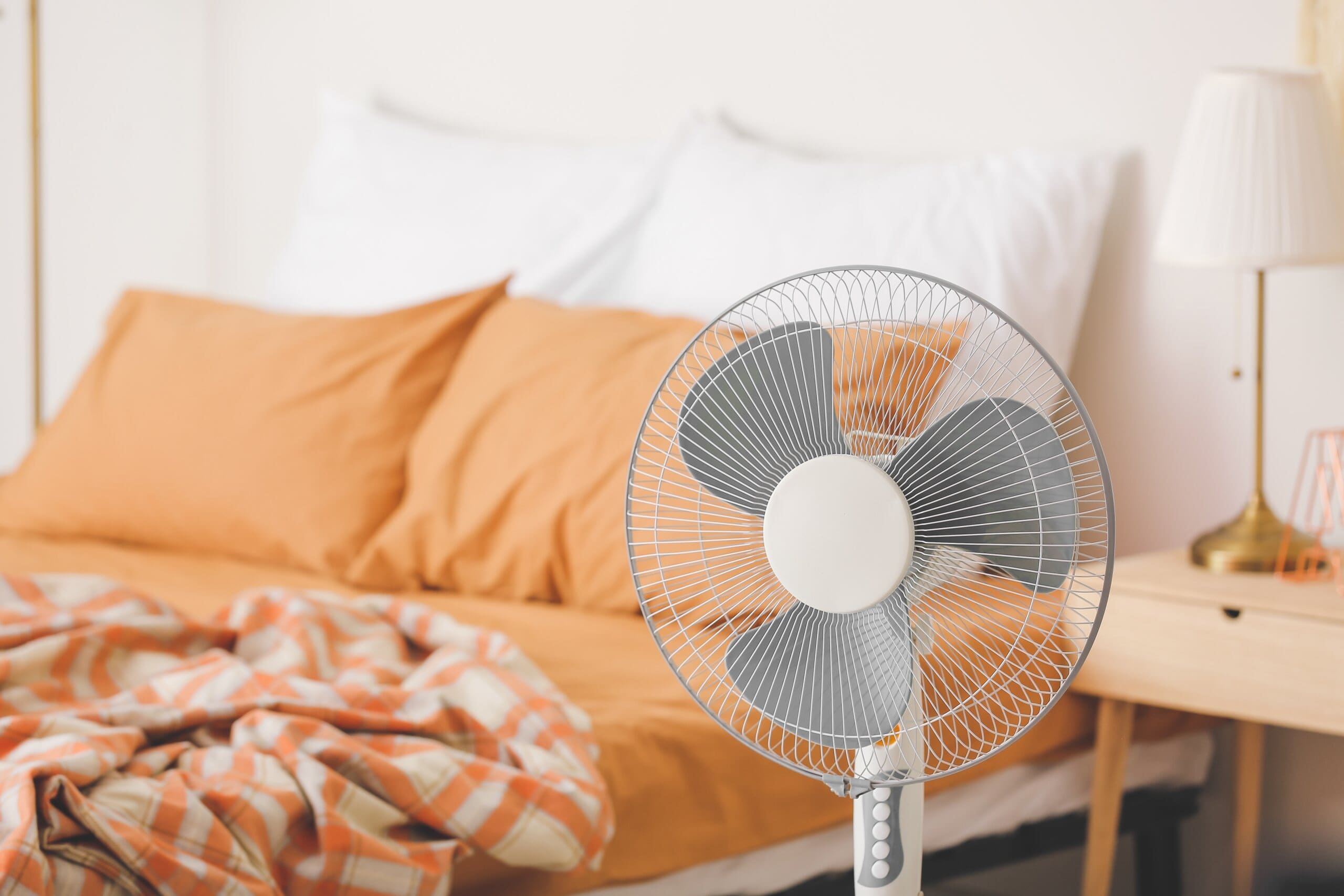 Modern electric fan in bedroom, next to a low bed with orange bedding.