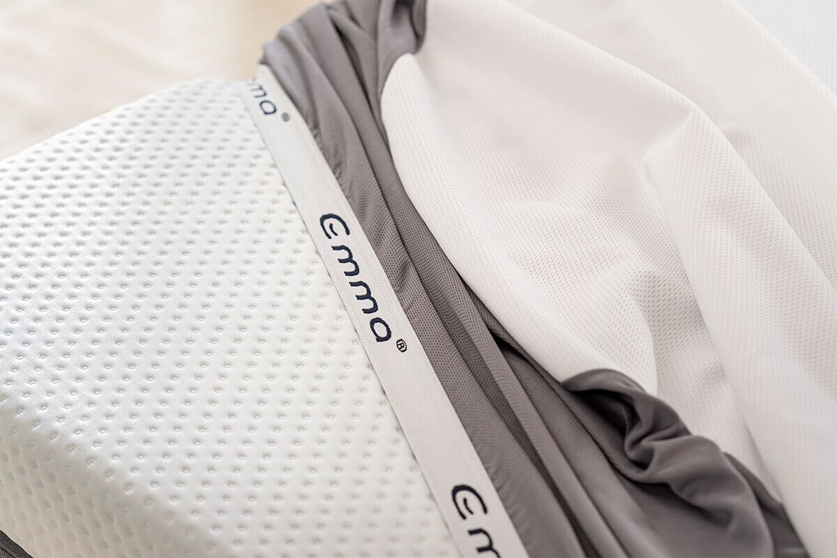Close up image of the corner of a mattress, with the emma waterproof mattress protector lifted to expose the mattress beneath.