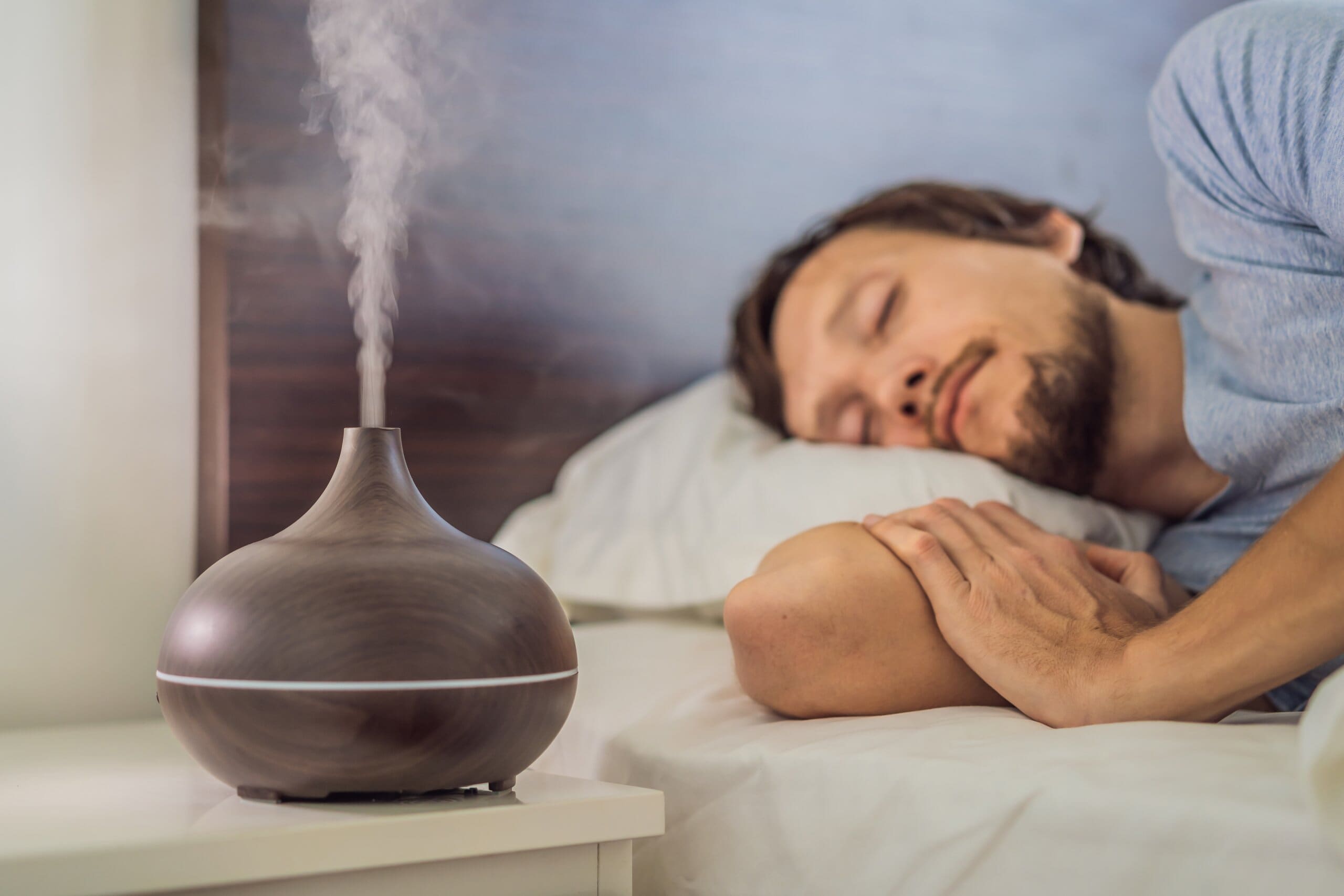 Man sleeping with essential oil diffuser on bedside table.