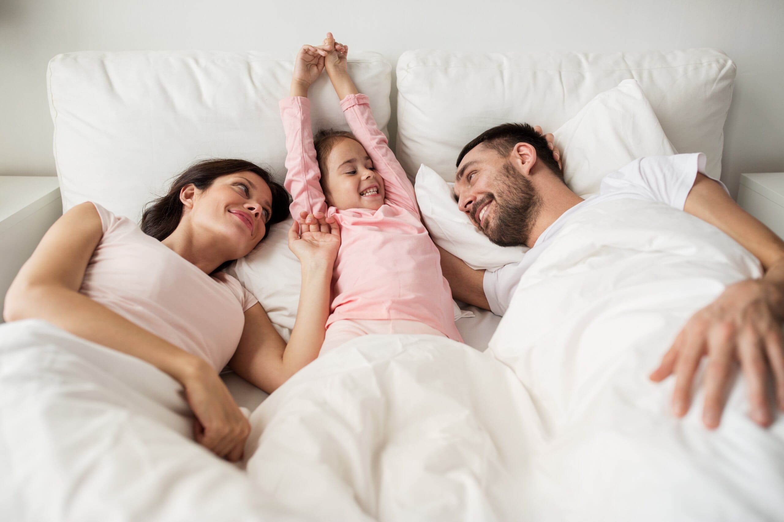 Couple and child stretching in a bed together.