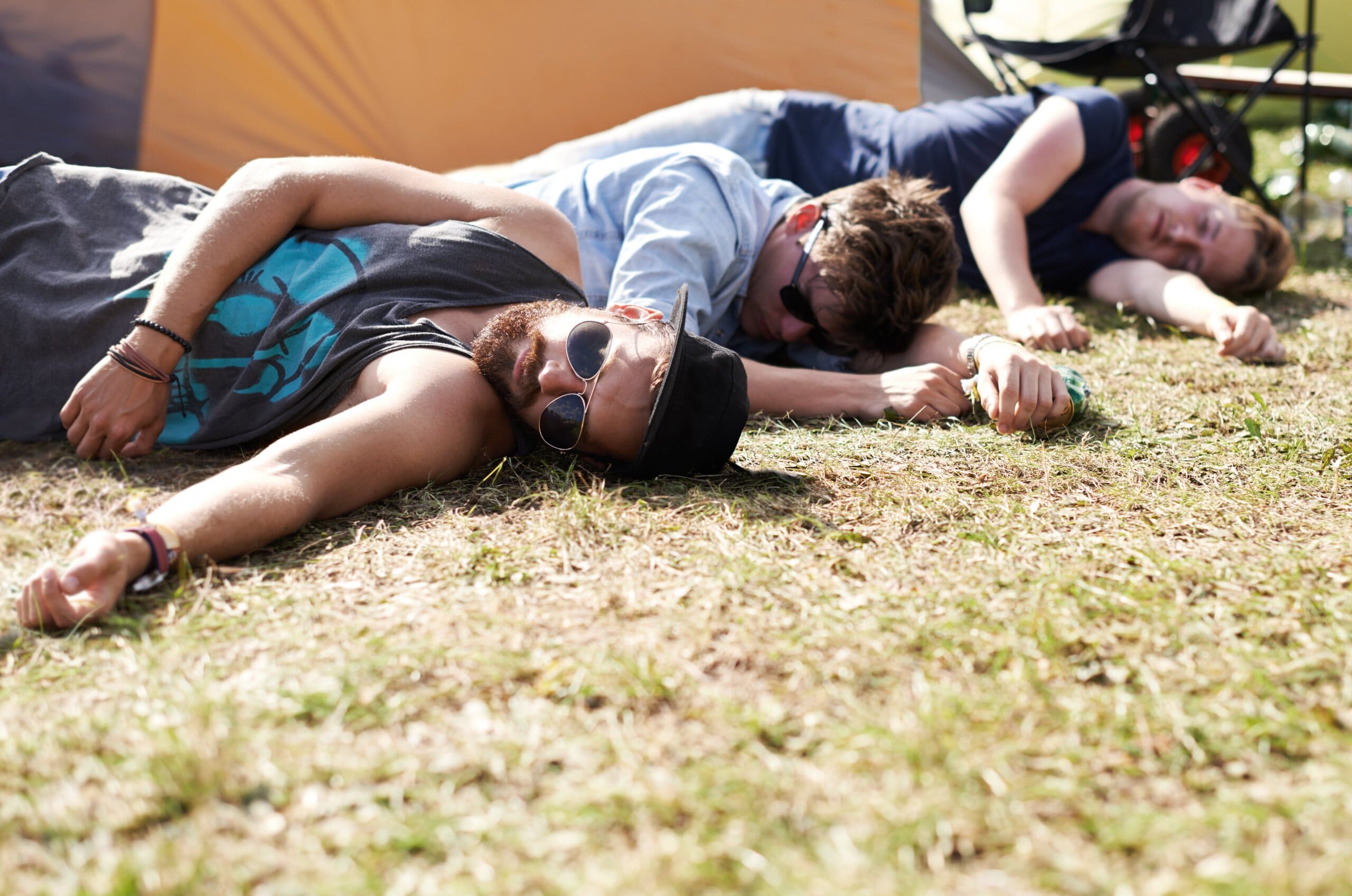 Three men laying down sleeping at a festival, hungover.