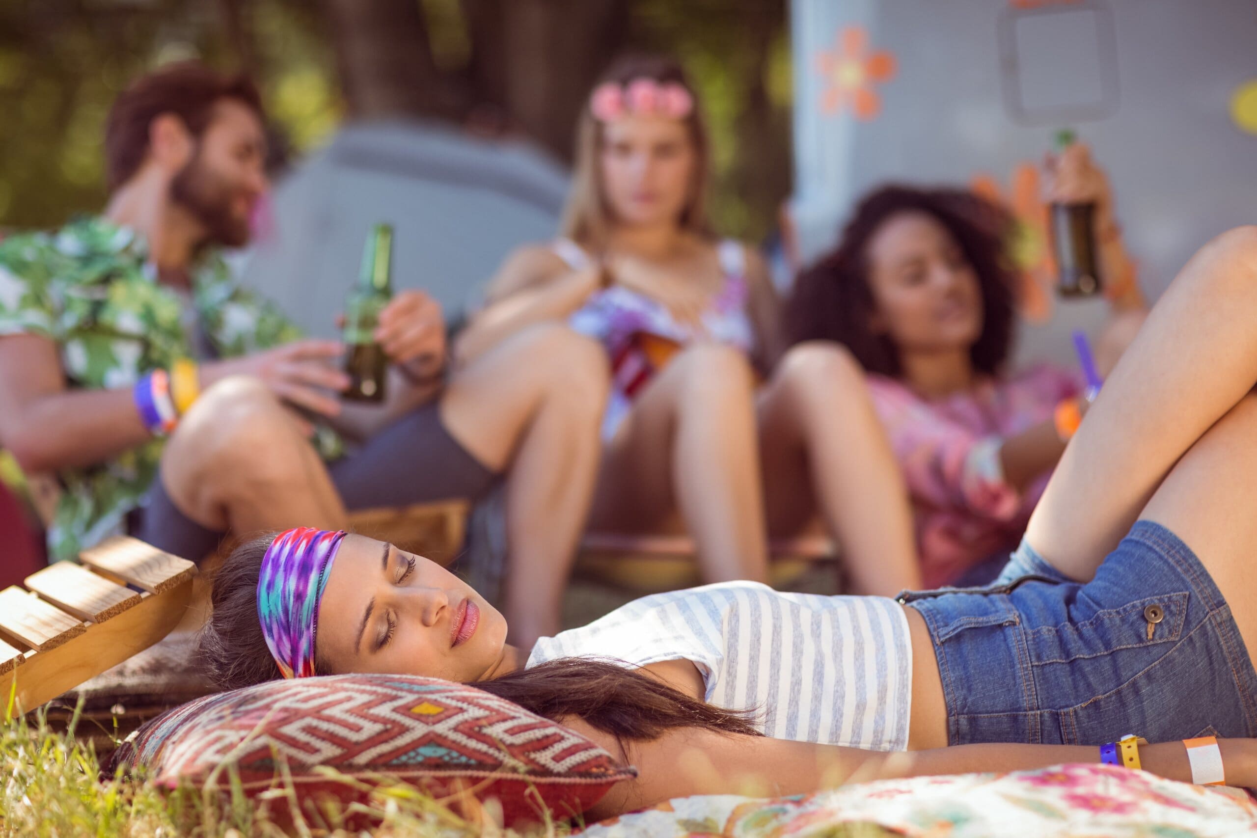 Girl sleeping on ground in front of a group of friends at a festival.