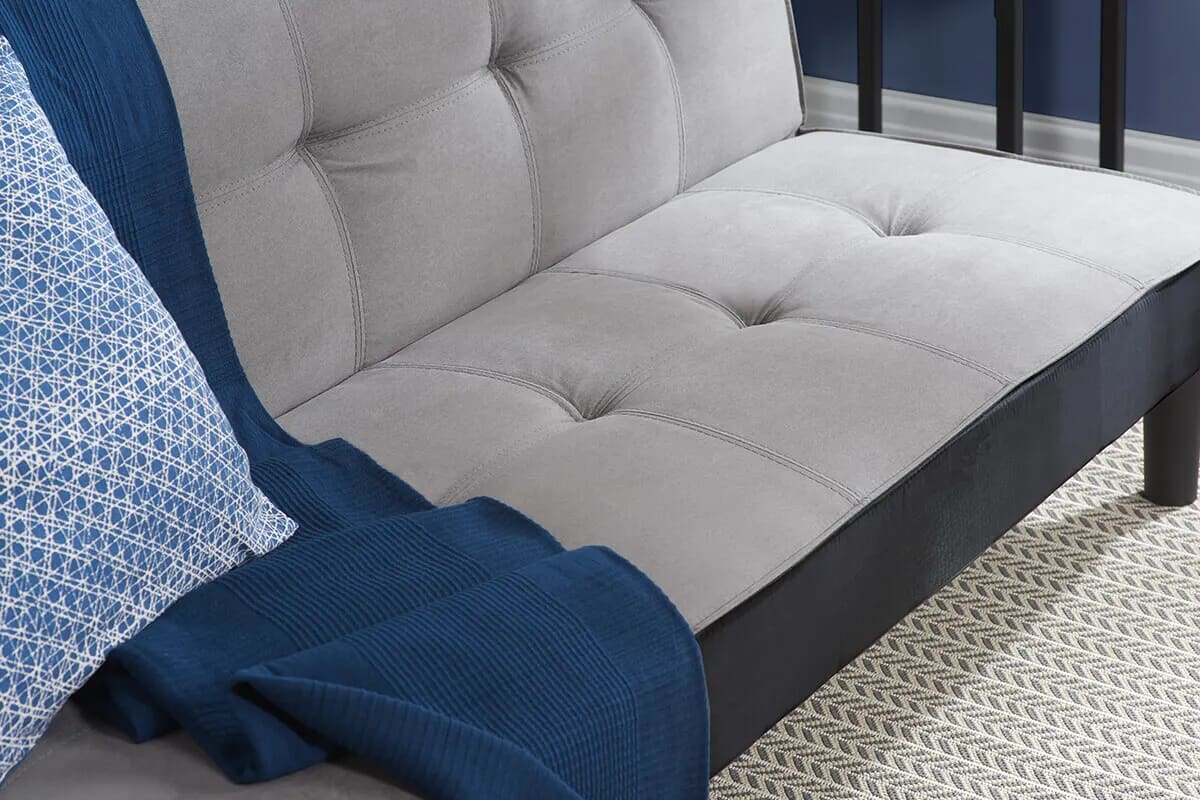 Close up image of grey tufted sofa bed with a blue blanket and light blue and white cushion.