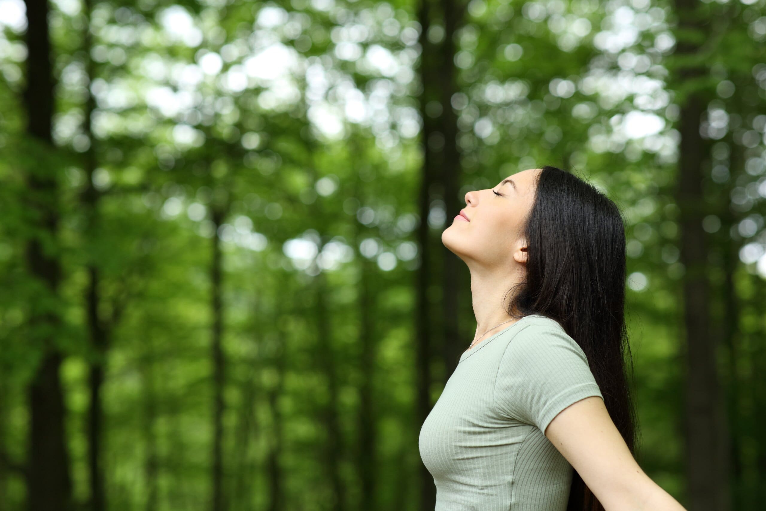 Woman stood in forest taking a deep breath.