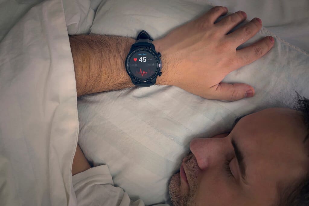 Close up of man asleep with his wrist wearing a heart rate sleep tracker.
