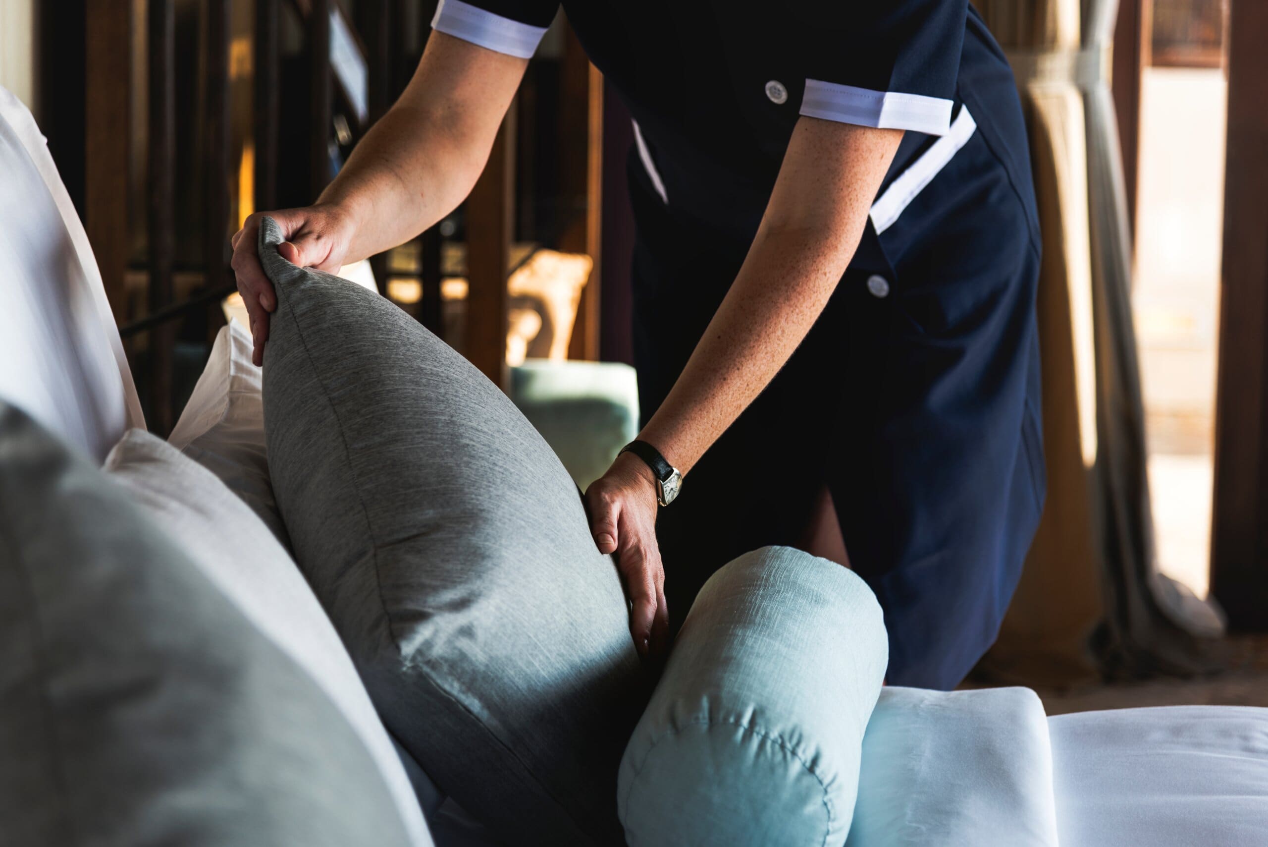 Cropped image of a housekeeper tidying pillows on a hotel bed.