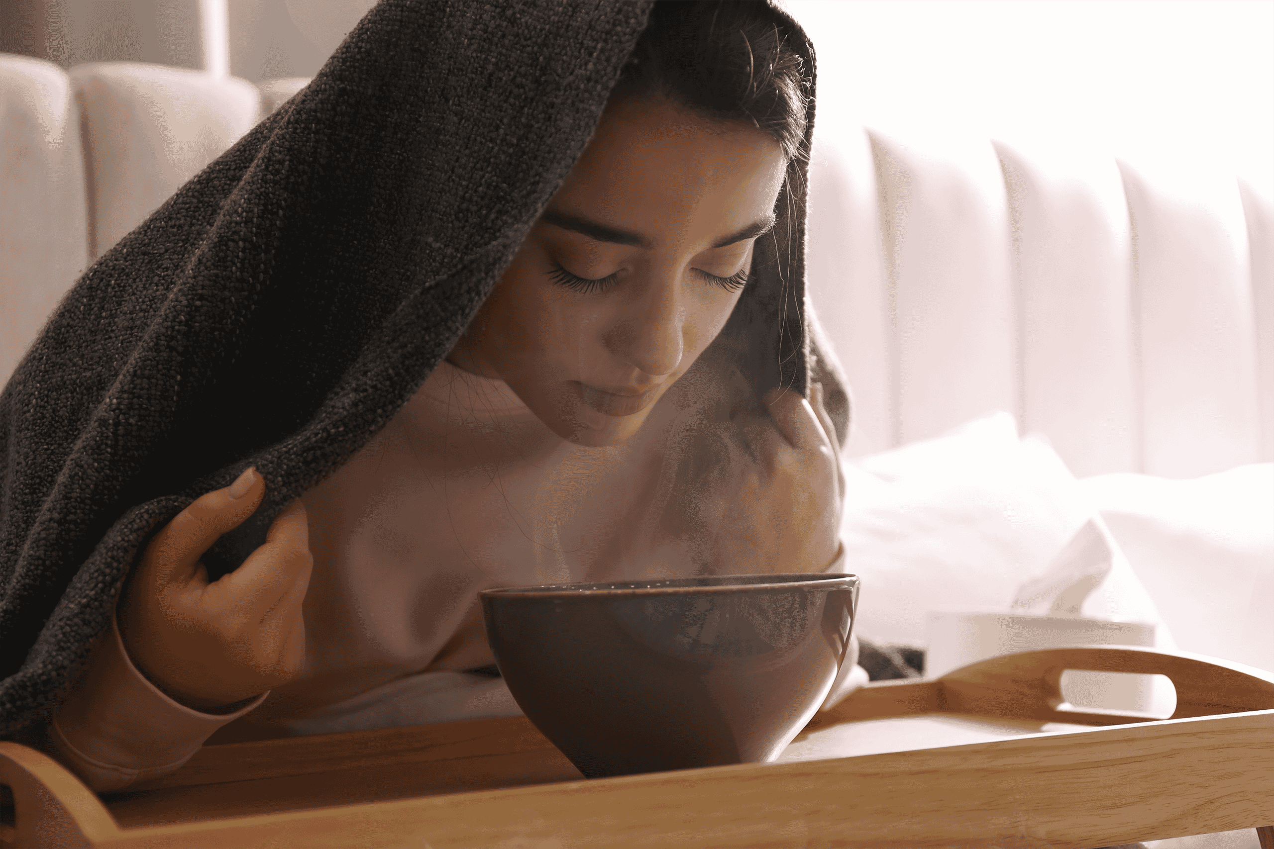 Woman with a towel over her head and face over a bowl of hot water, inhaling the steam.