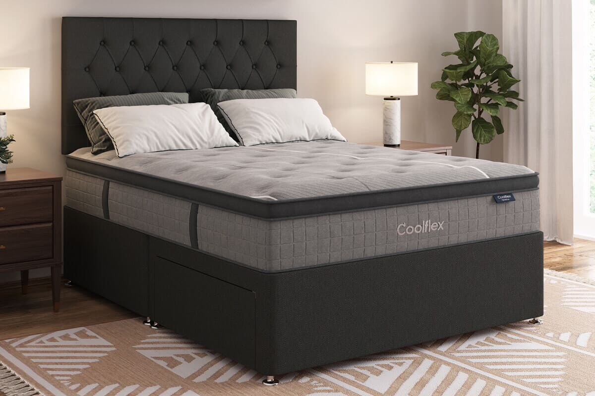 An image of the grey Hybrid Ice mattress on a black divan bed. It is unmade, but has pillows at the top end. It is placed in a neutral coloured bedroom.
