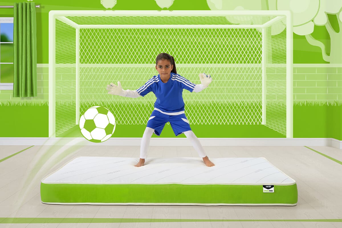 Image of a young girl in a football kit catching a football white standing on a Jay-Be anti allergy kids mattress.