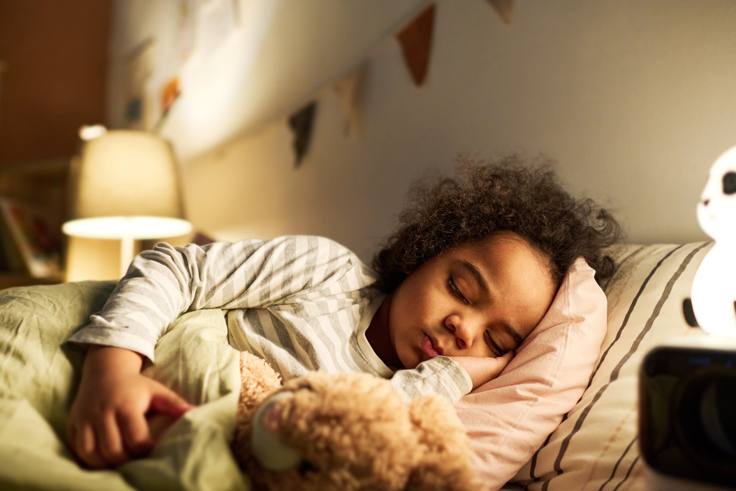 Small child asleep cuddling a teddy bear in bed.
