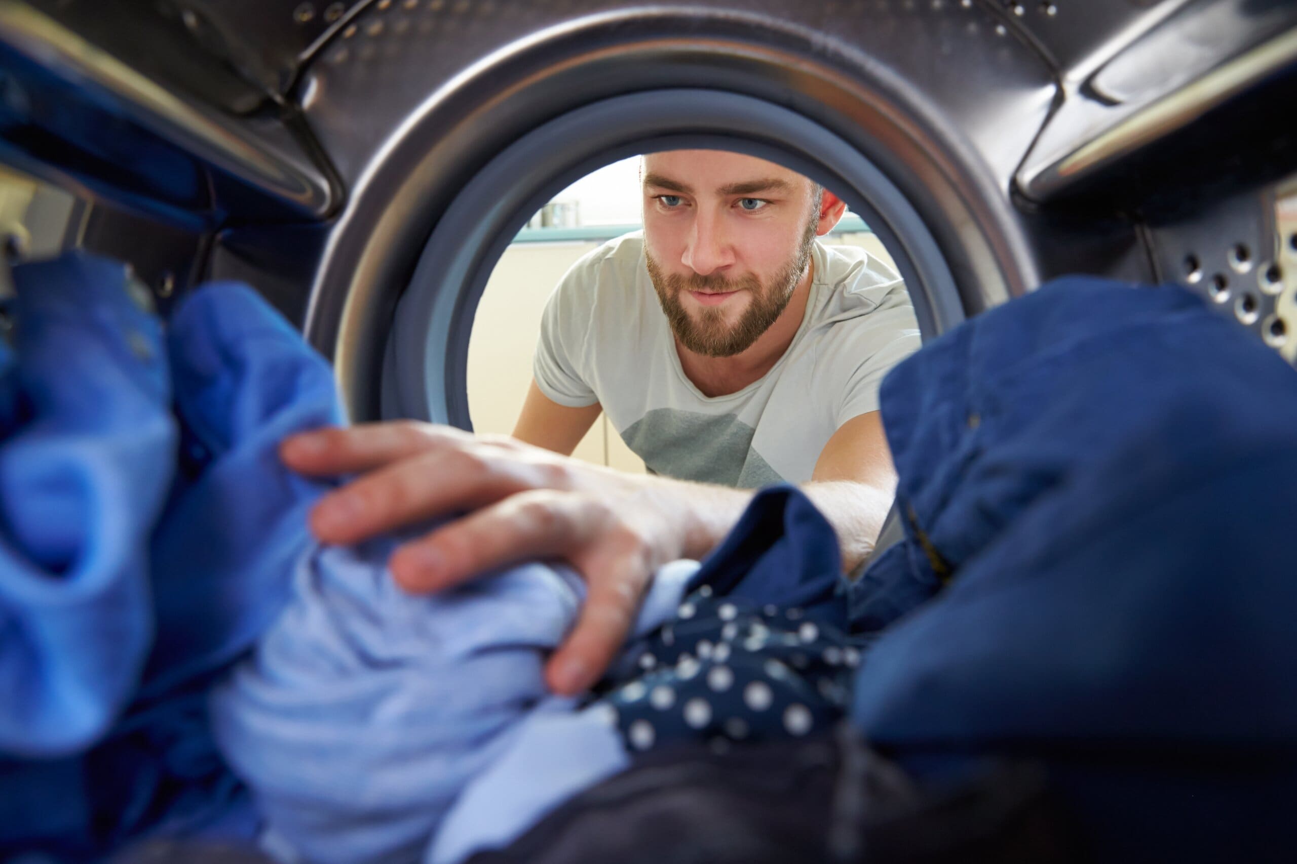 Man Doing Laundry Reaching Inside Washing Machine.