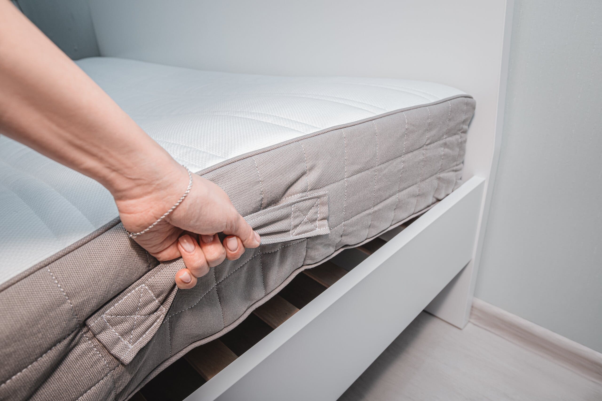 Hands lifting a mattress by the turning handles.
