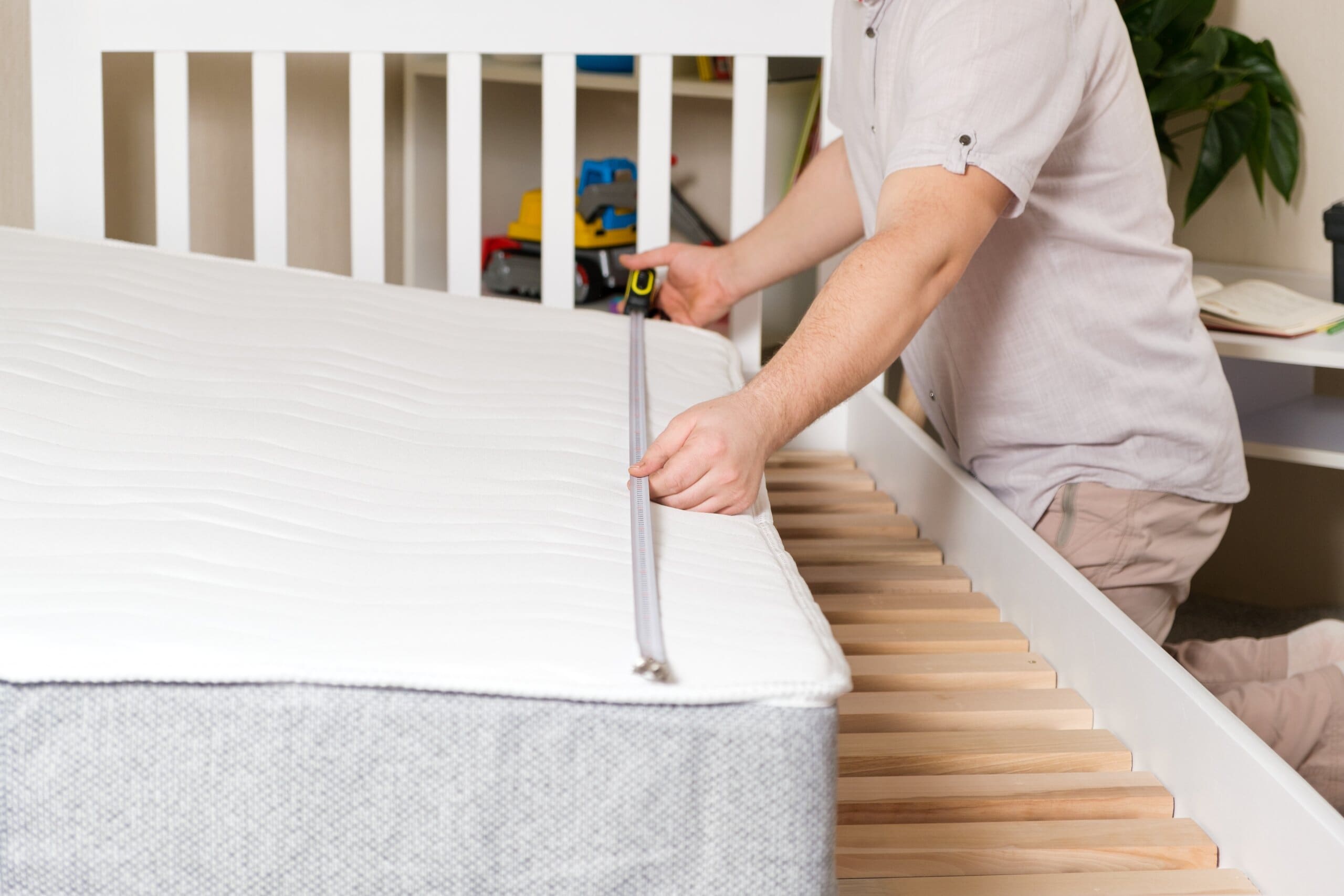 Man using tape measure to measure the length of a mattress sat on a bed frame.
